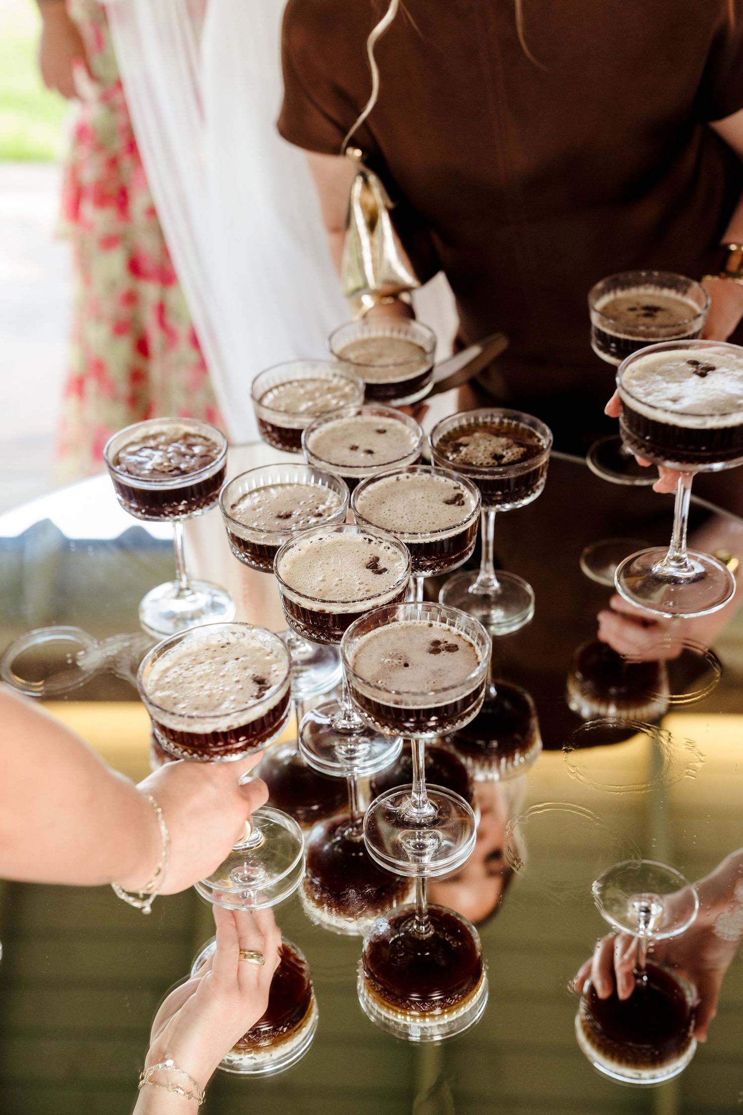Espresso martini cocktails arranged on a mirrored tray being served to wedding guests at a reception.