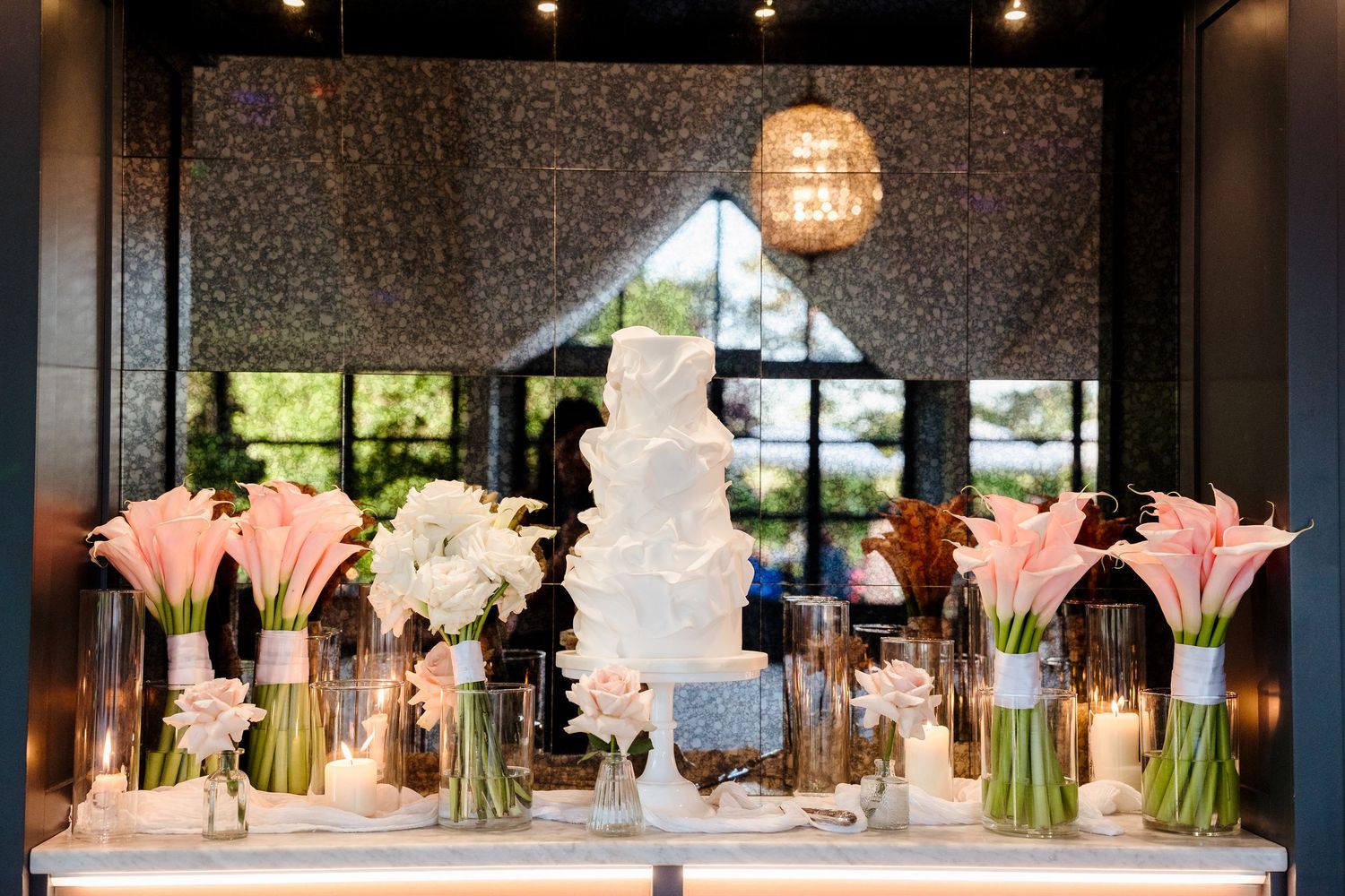Elegant white wedding cake surrounded by pink calla lilies and white florals with candles.