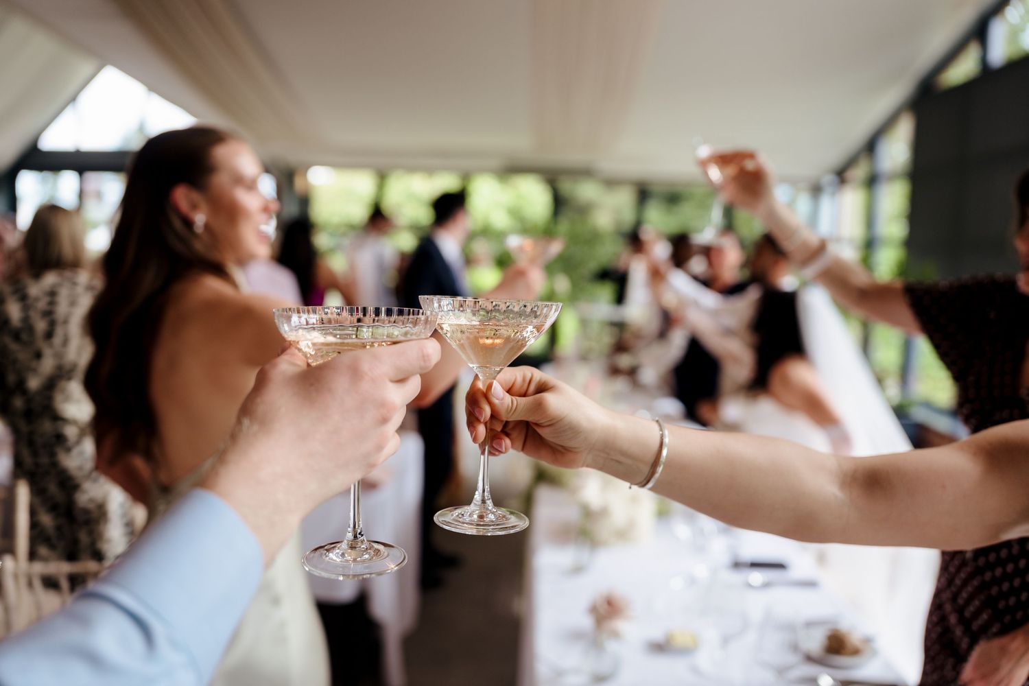 Wedding guests clinking champagne coupe glasses in celebratory toast at elegant reception venue.