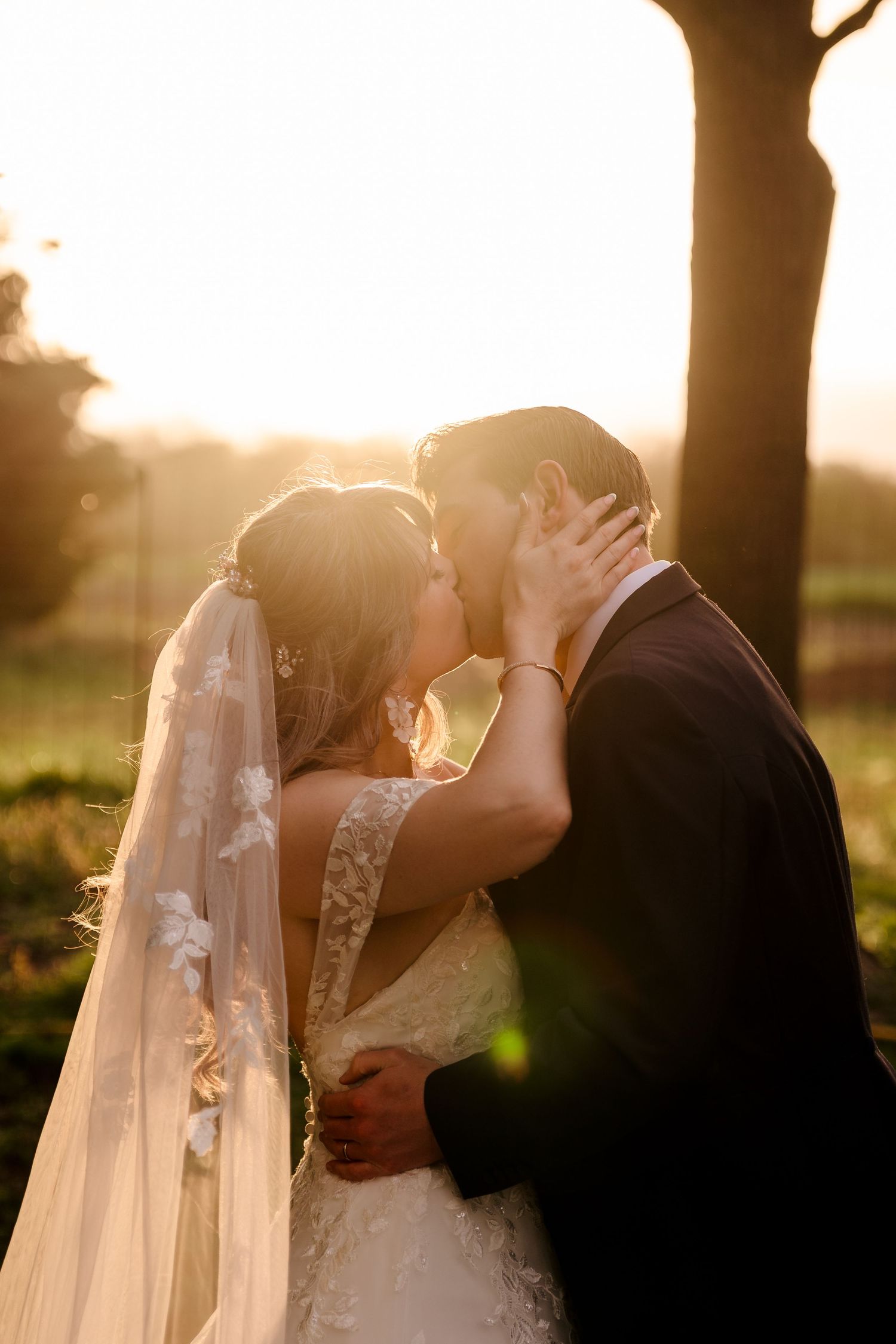 Bride and groom sharing a romantic kiss bathed in golden sunset light outdoors.