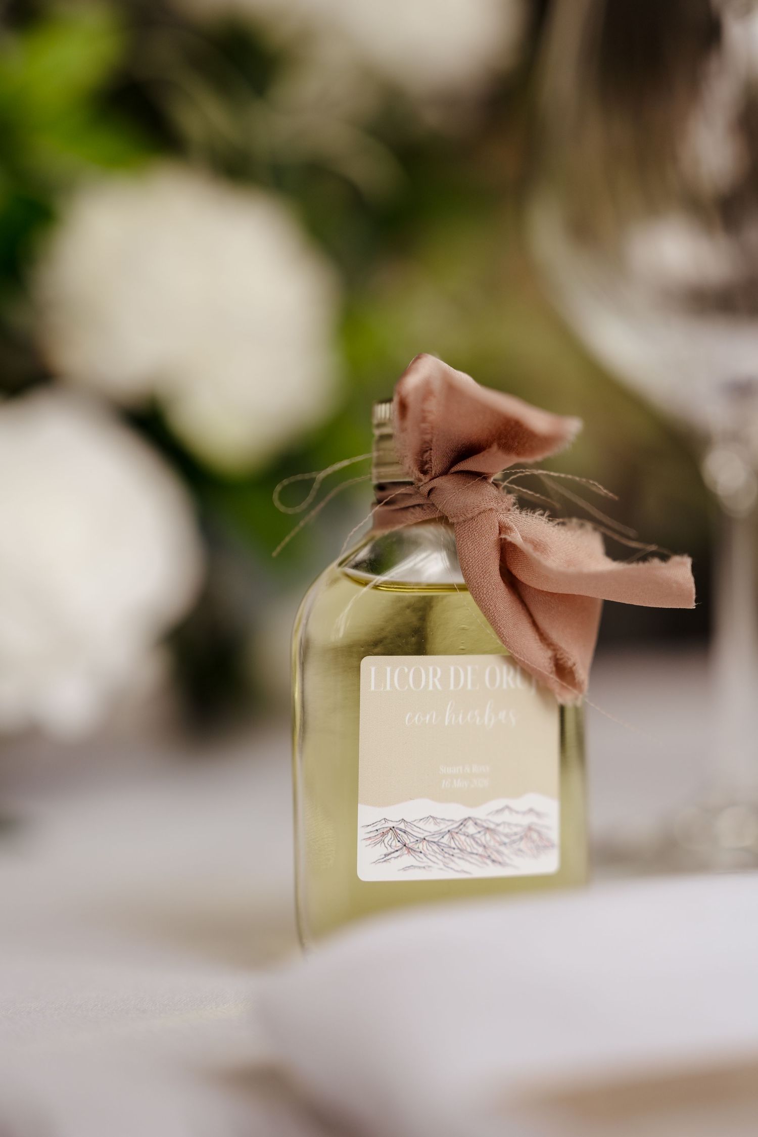 Elegant bottle of Licor de Oro tied with dusty rose ribbon bow as wedding table favor.