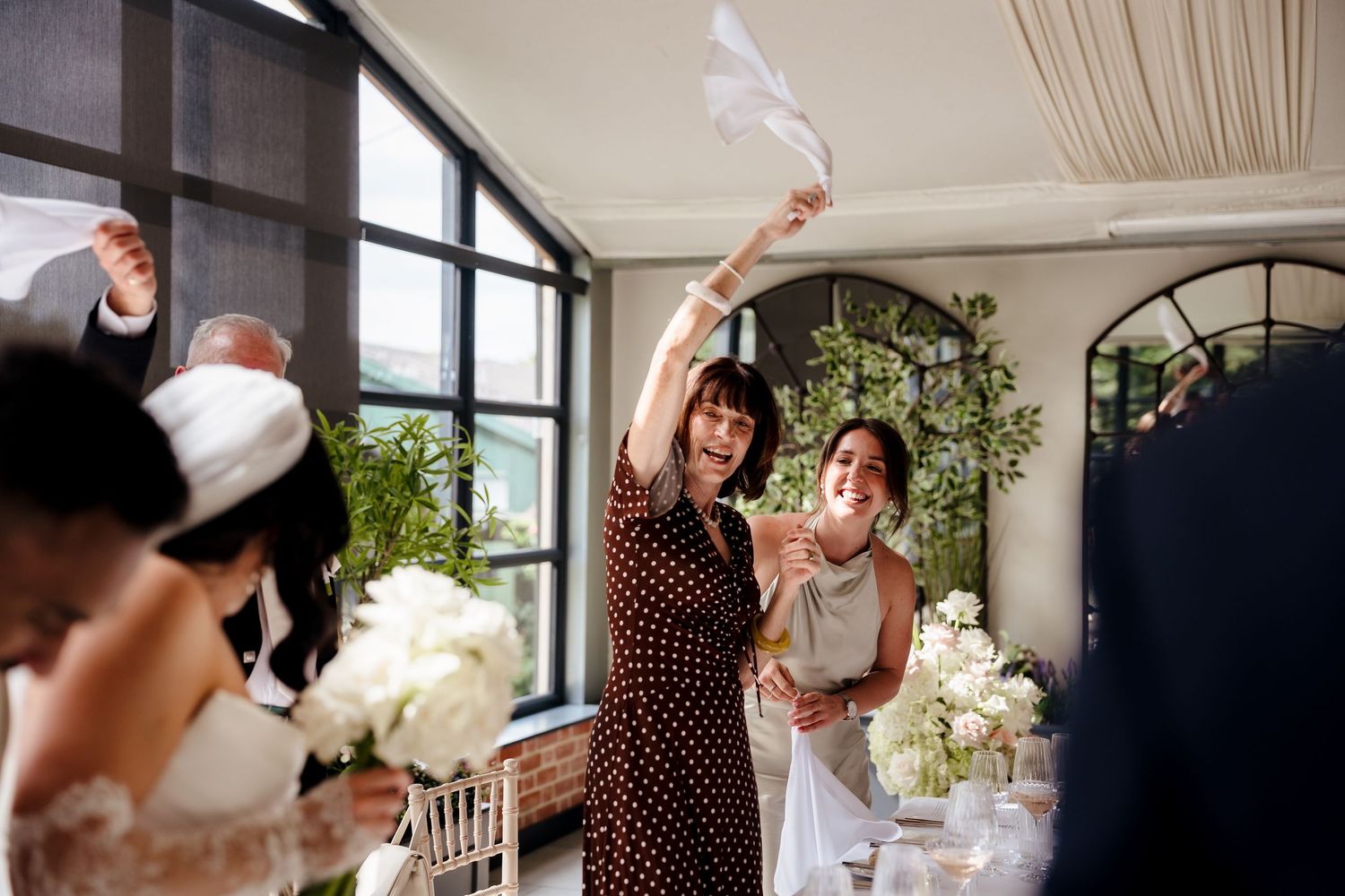 Excited wedding guest waves white napkin in celebration as bride enters indoor wedding reception.