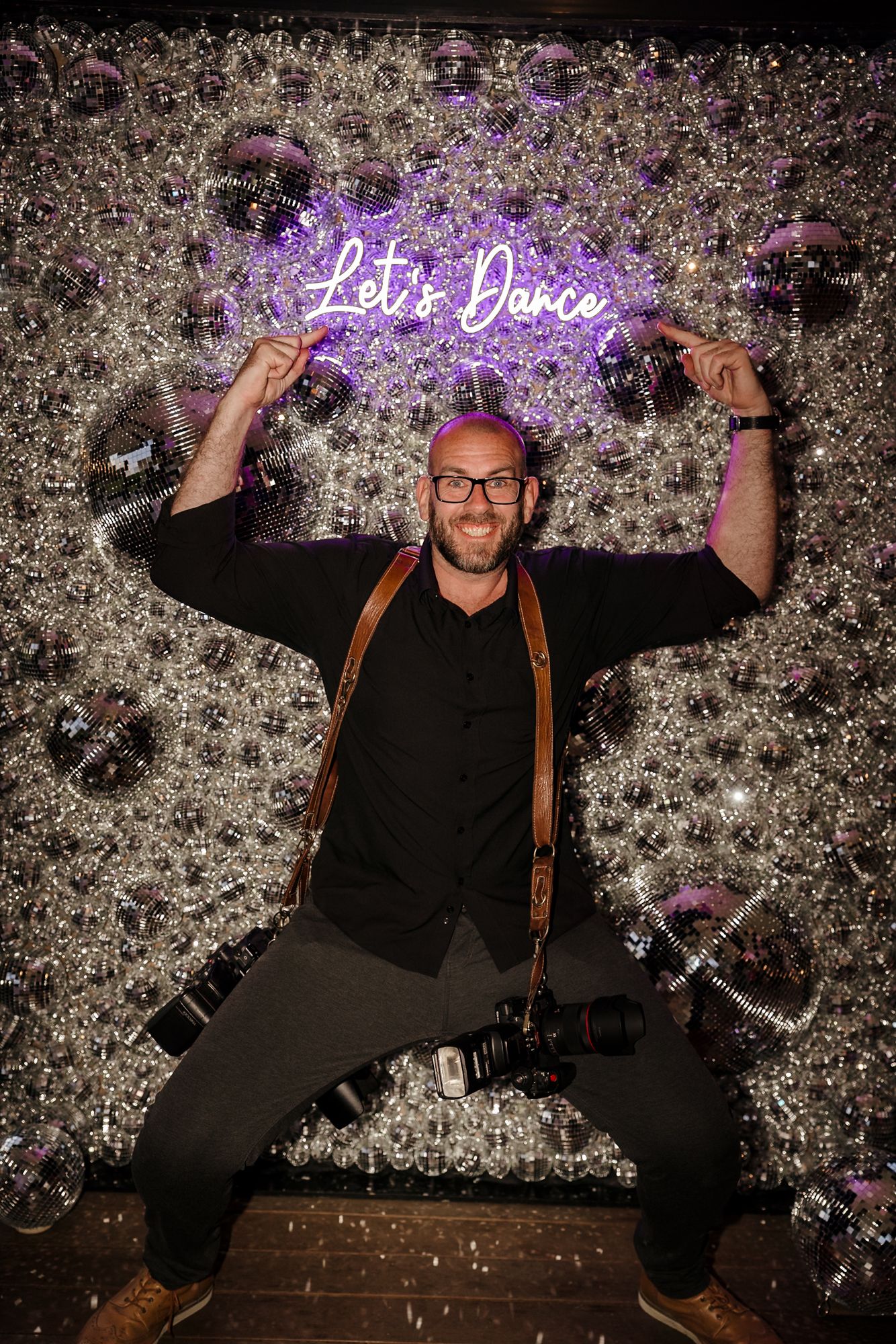 Man posing in front of a glittery wall with a purple neon 