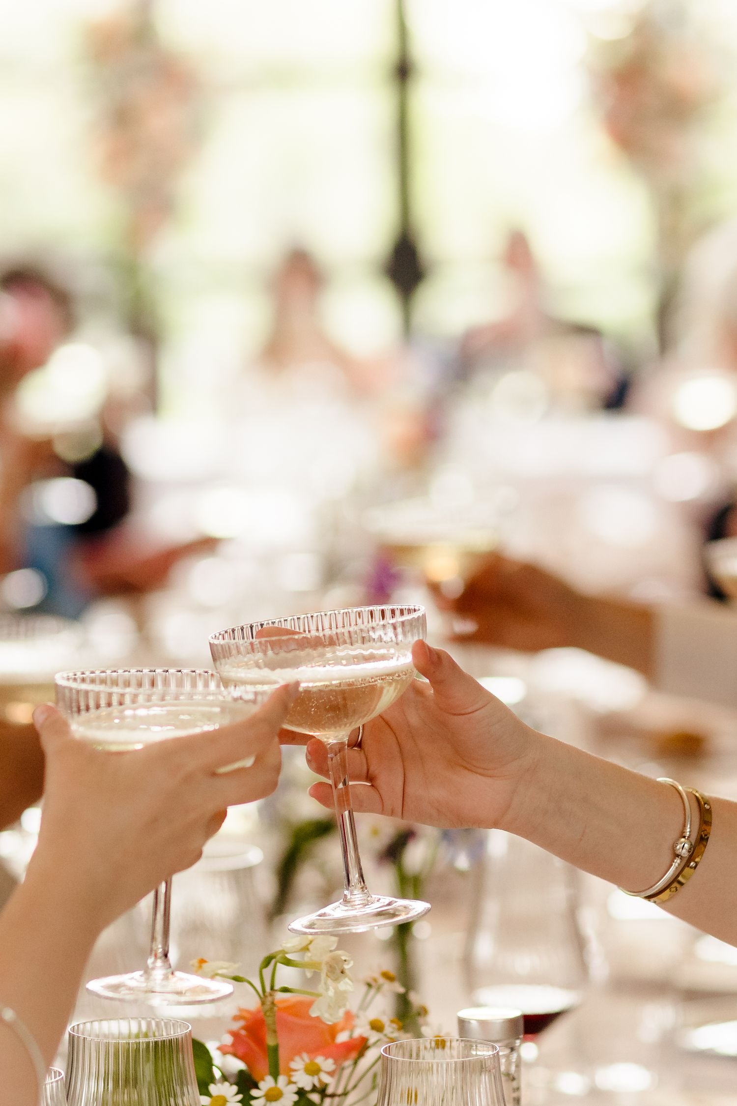 Guests clinking champagne coupe glasses in toast at elegant outdoor wedding reception.