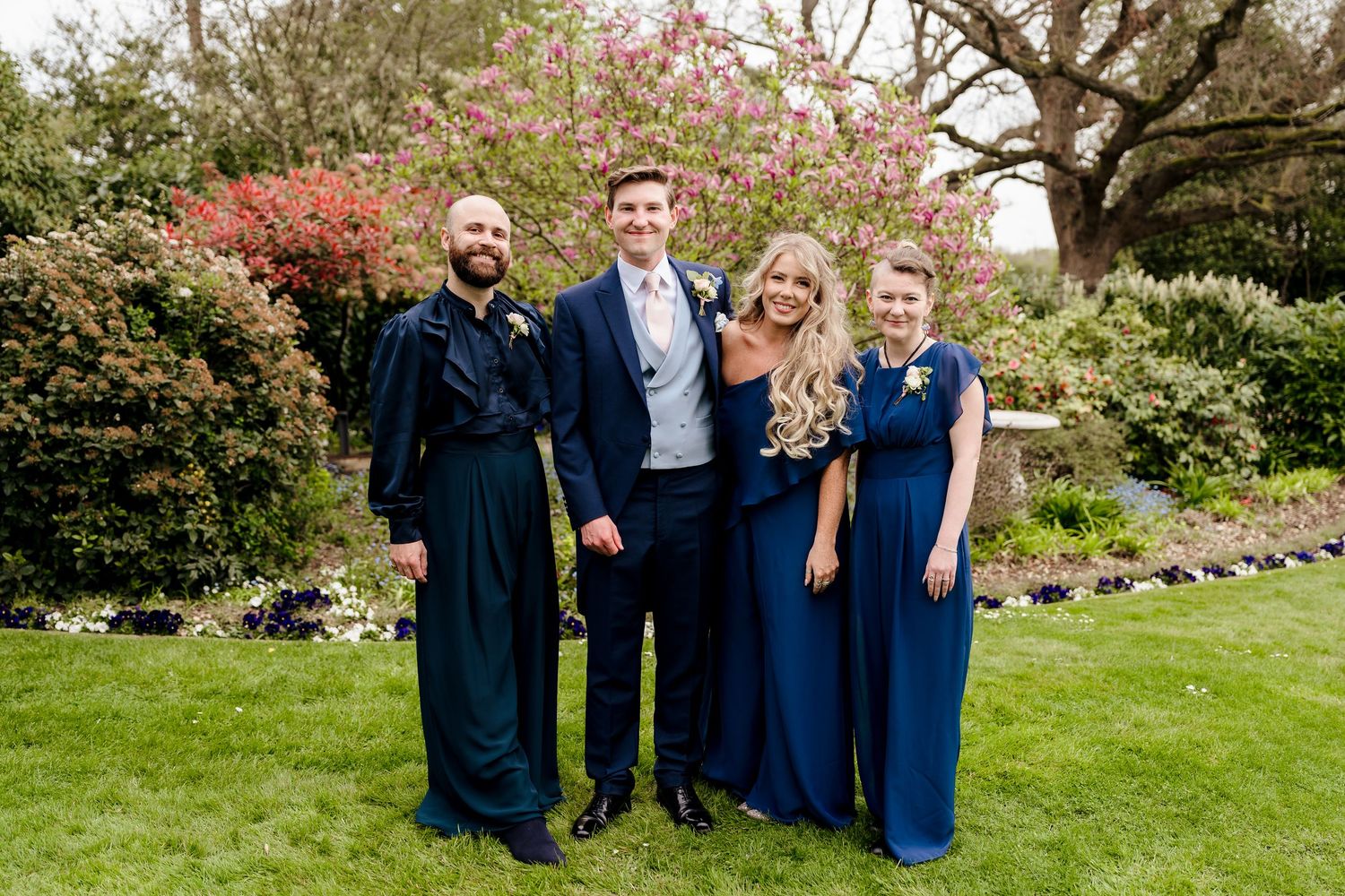 Groom in navy suit posing with three bridesmaids in navy dresses before flowering magnolia tree.