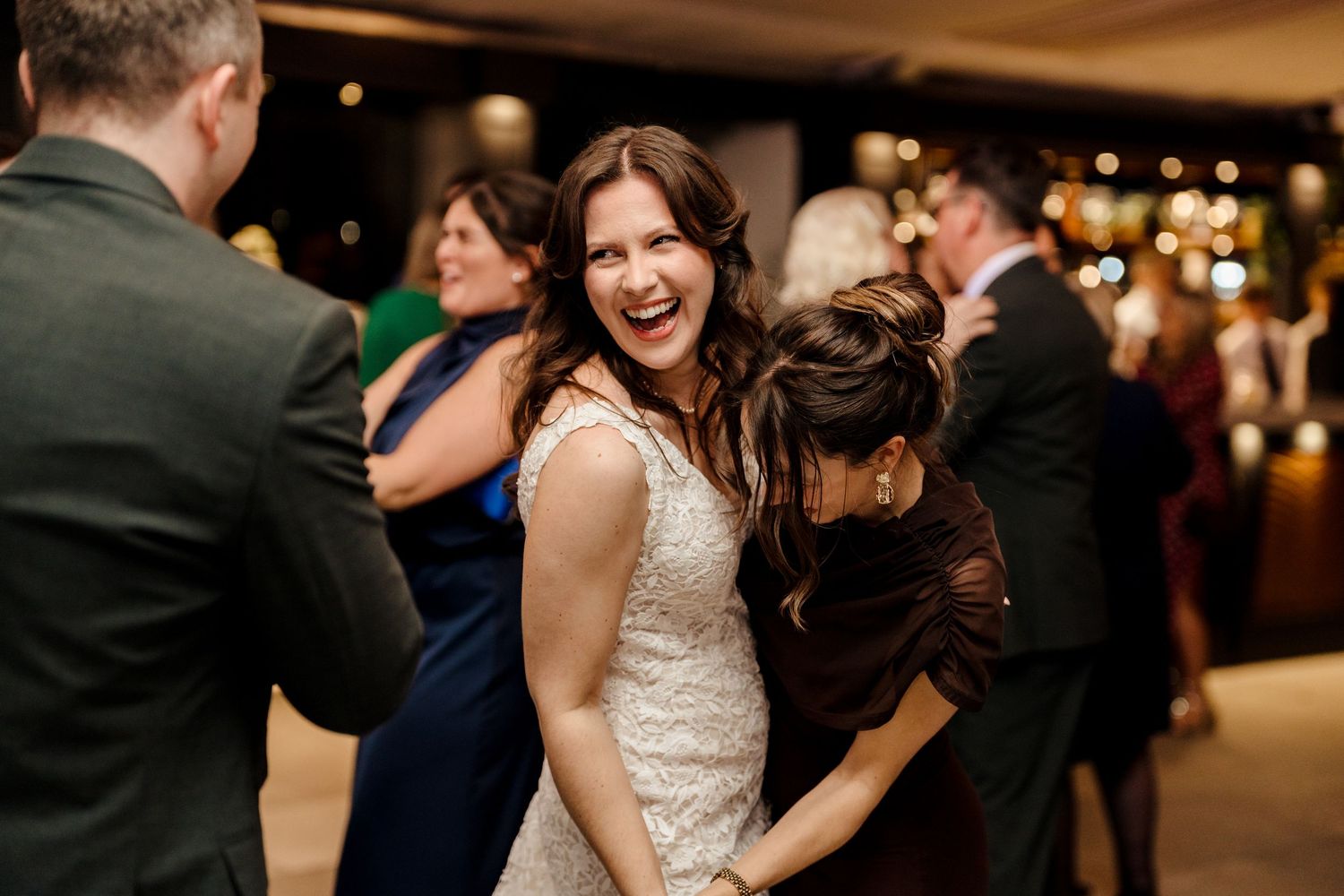 Laughing bride hugging a guest while dancing joyfully at her wedding reception.