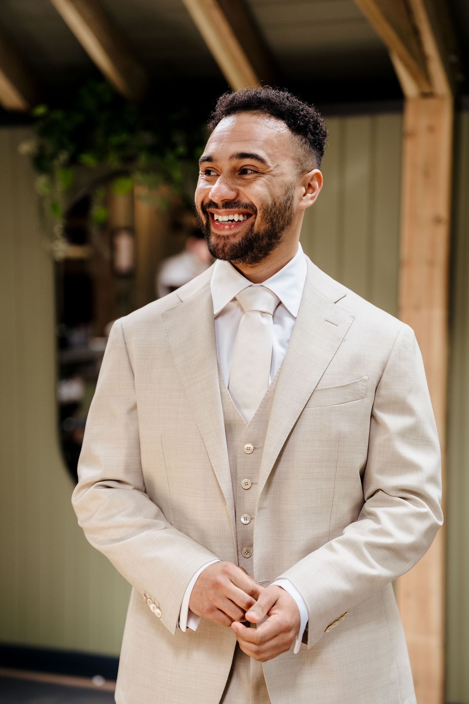 Smiling groom in a beige suit and tie buttoning his jacket before the wedding ceremony.
