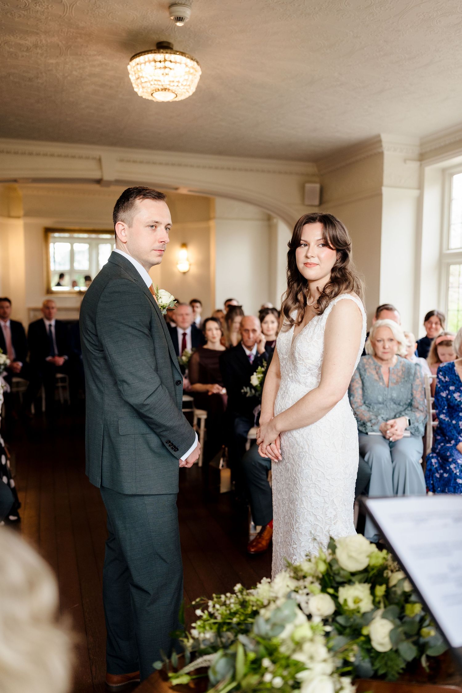 Bride and groom holding hands during their wedding ceremony with guests seated behind them.