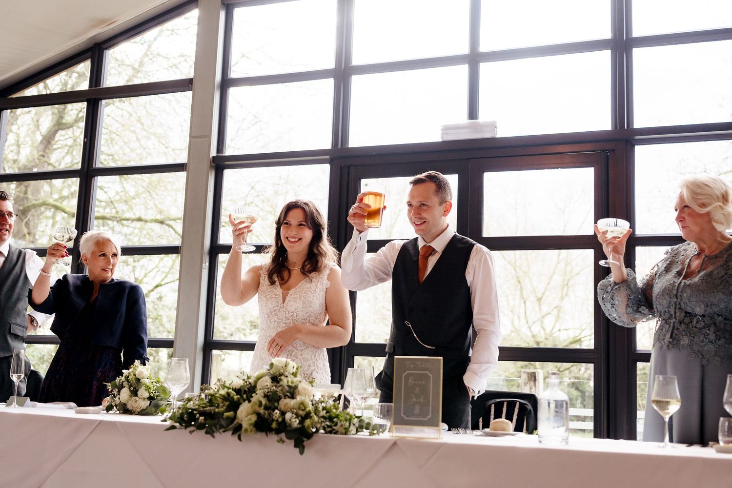 Bride and groom raise glasses in wedding toast with guests at elegant reception venue.