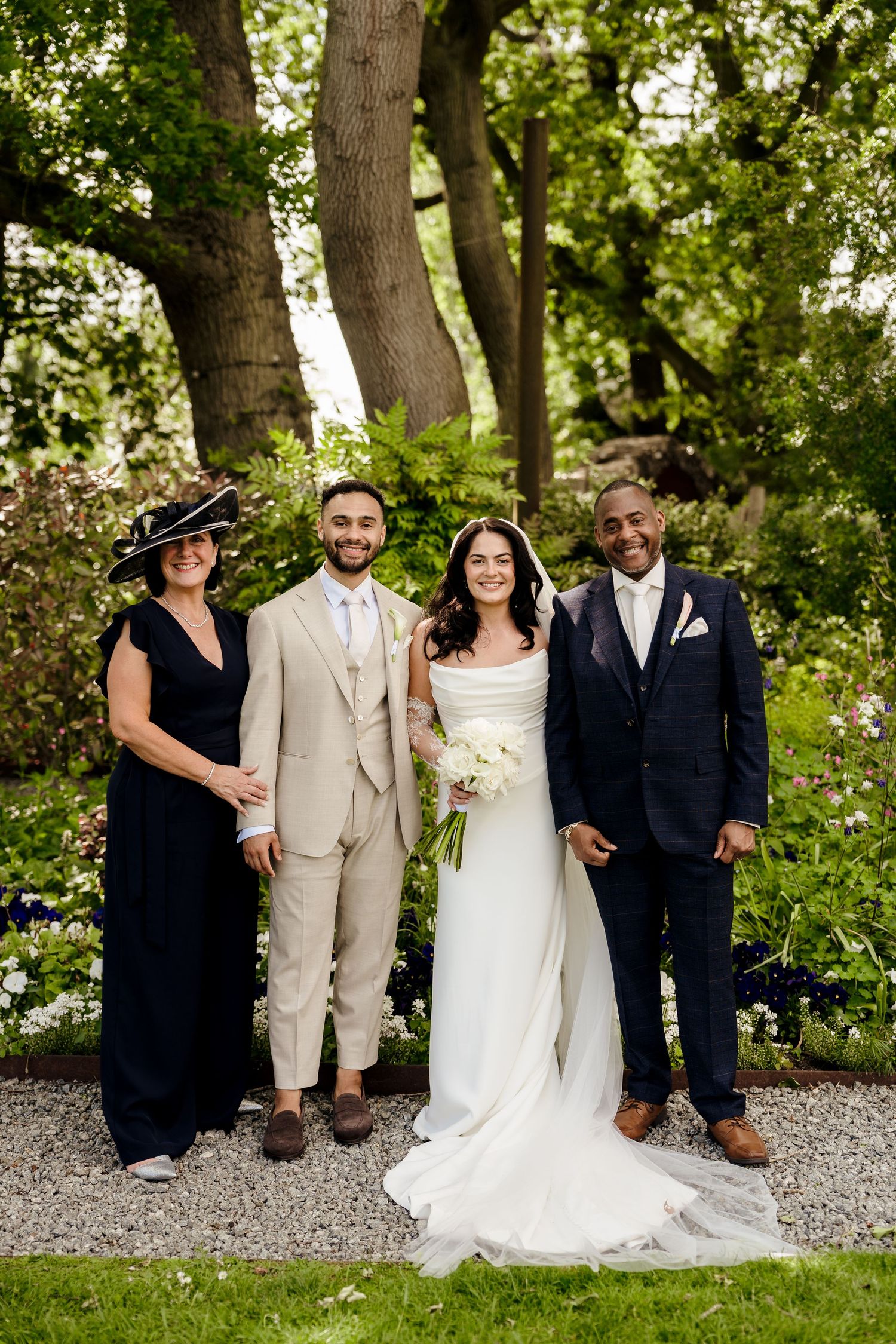 Bride and groom posing with two family members in a lush garden wedding setting.