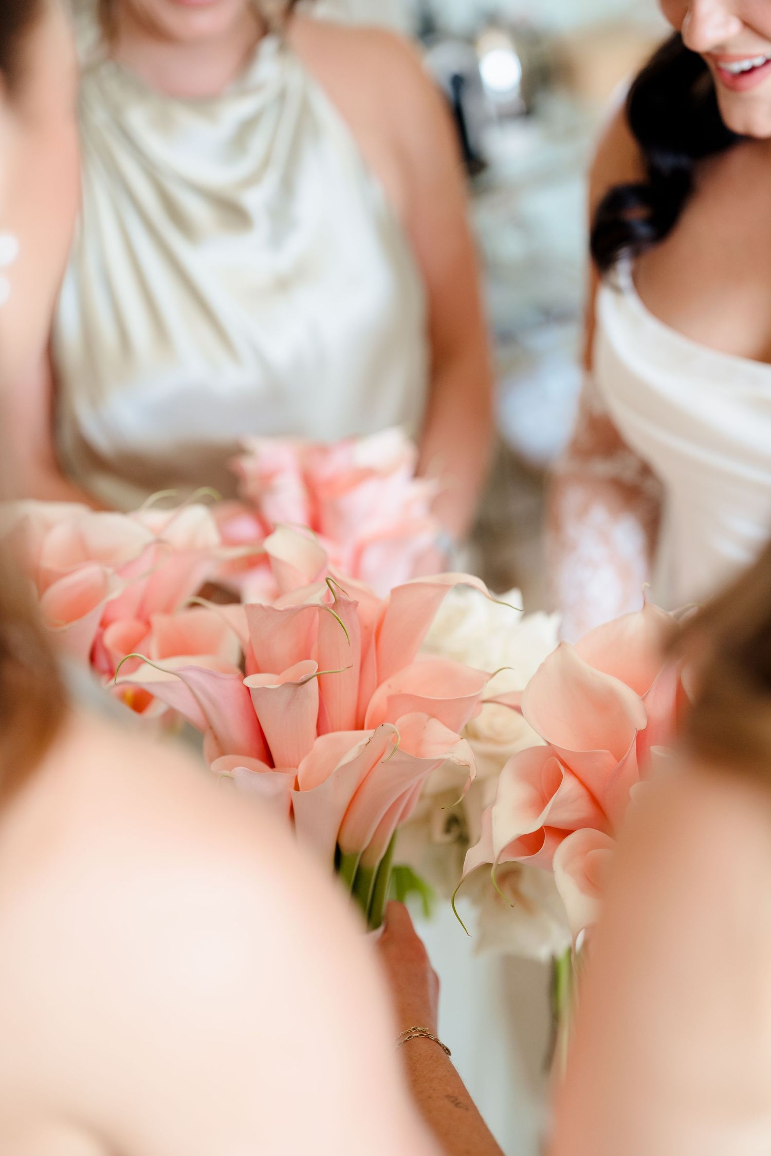 Close-up of bridesmaids holding elegant pink calla lily bouquets at a wedding celebration.