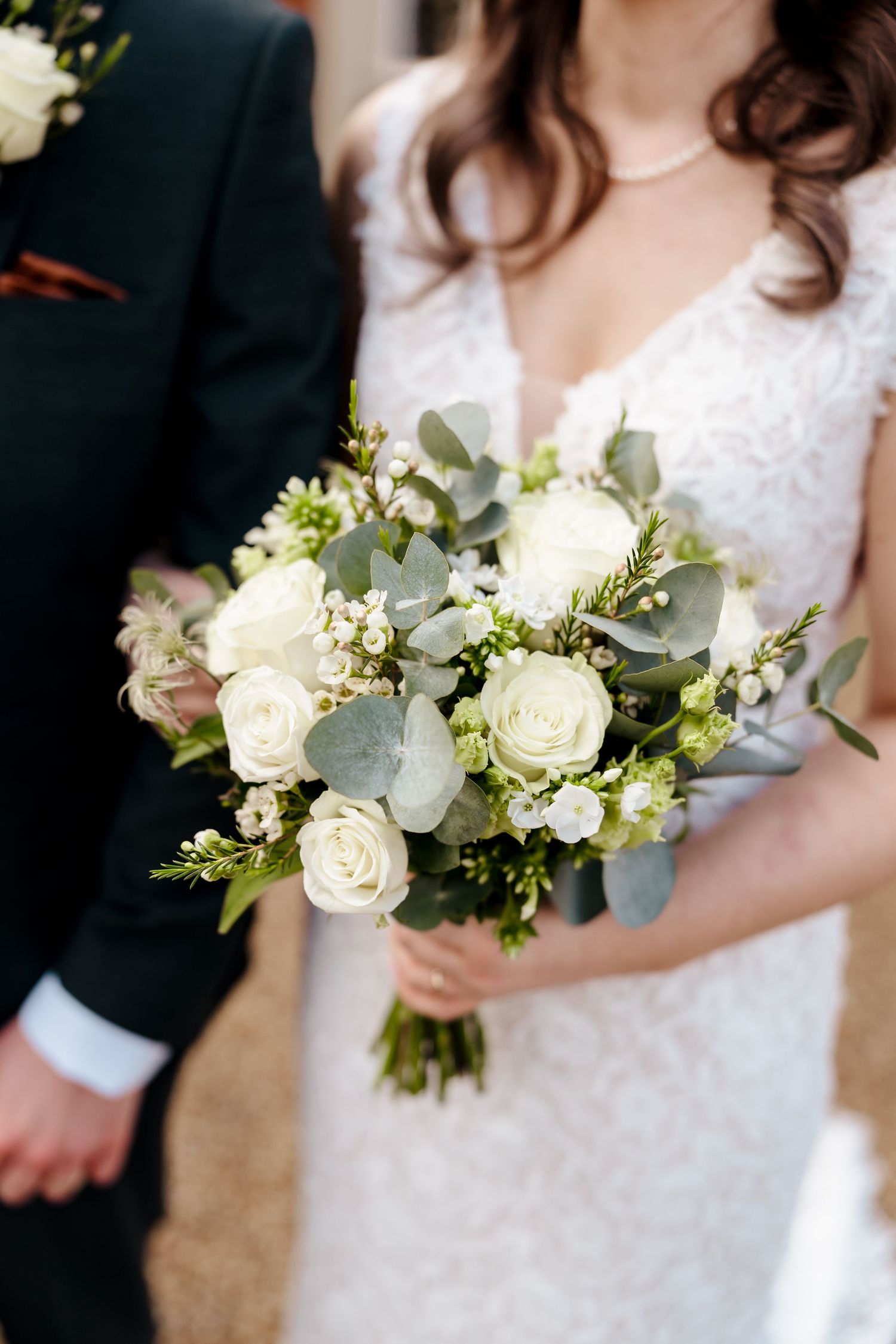Close-up of bridal bouquet with white roses and eucalyptus held by bride in lace gown.