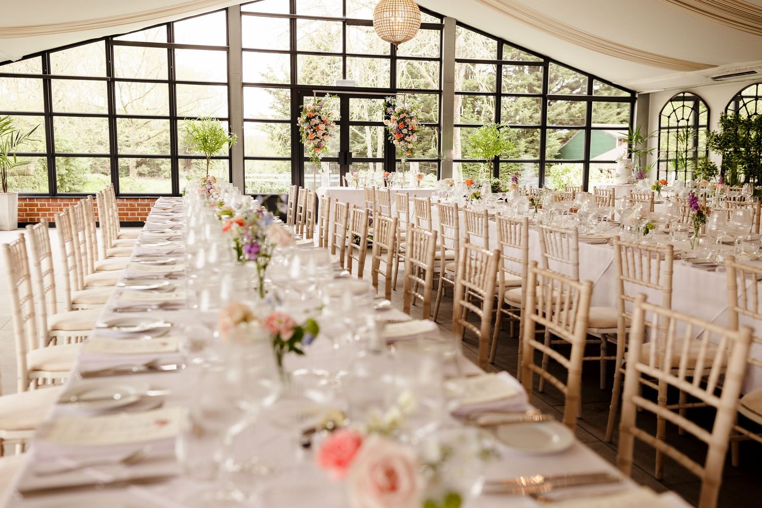 Bright wedding reception hall with long banquet tables, chiavari chairs and floral centerpieces.