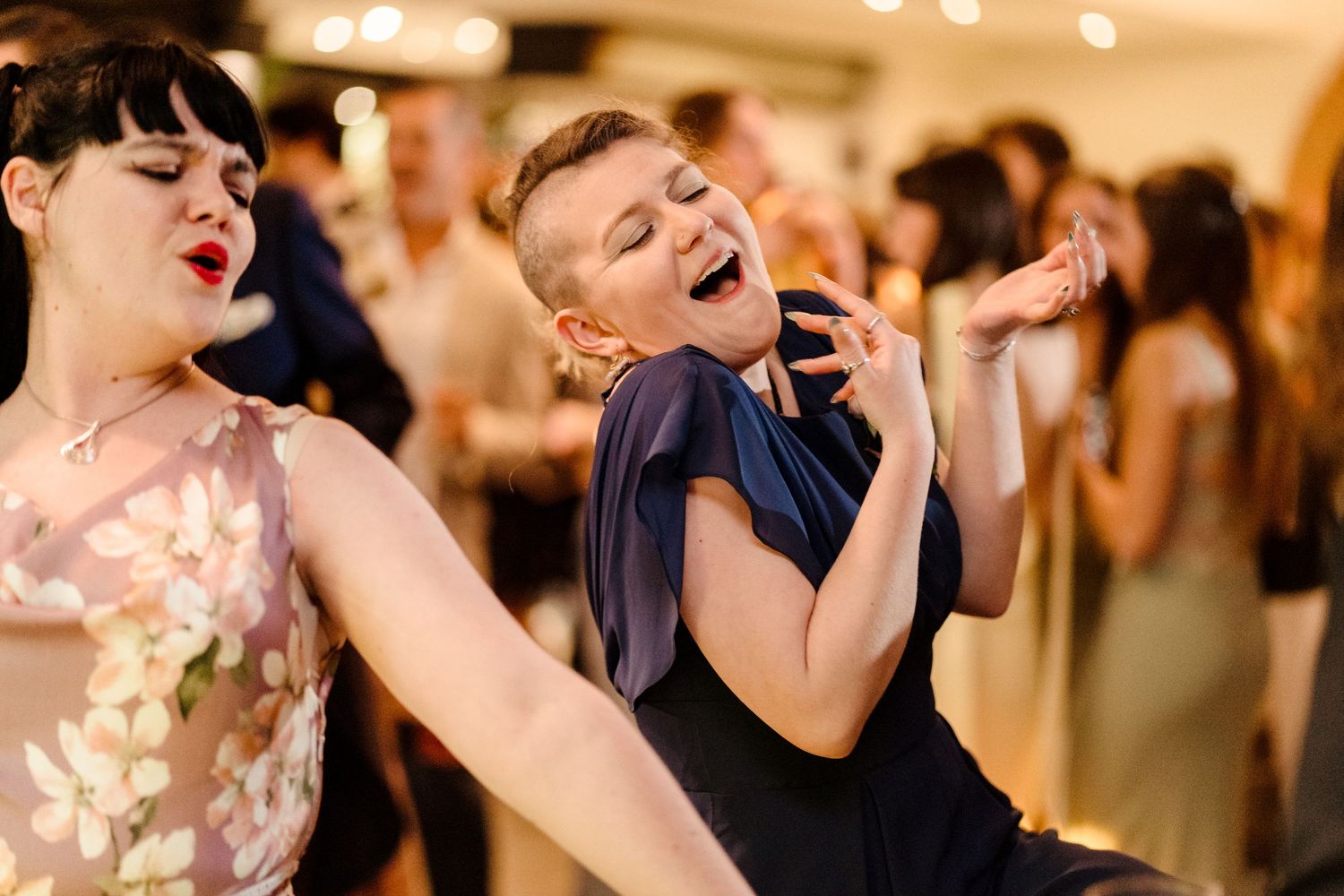 Two women dancing and singing joyfully on a wedding reception dance floor.