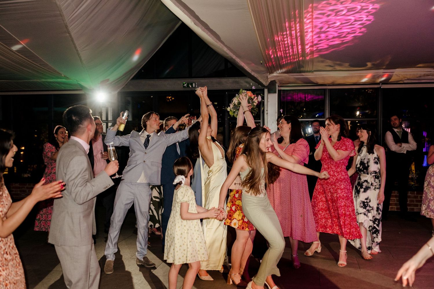 Excited wedding guests reaching up to catch the bridal bouquet toss at a lively reception party.