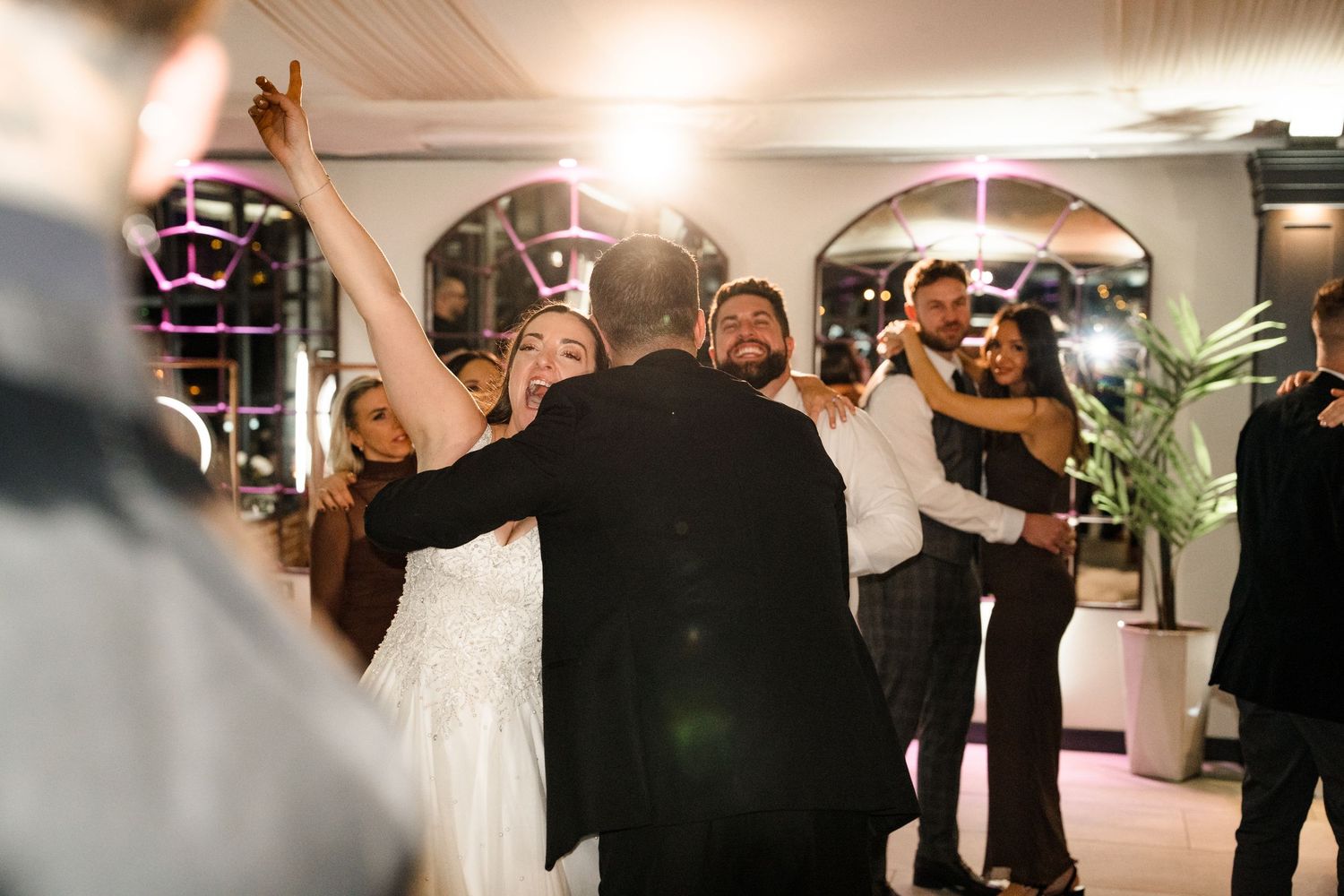 Bride and wedding guests dance joyfully together on the dance floor at evening wedding reception.