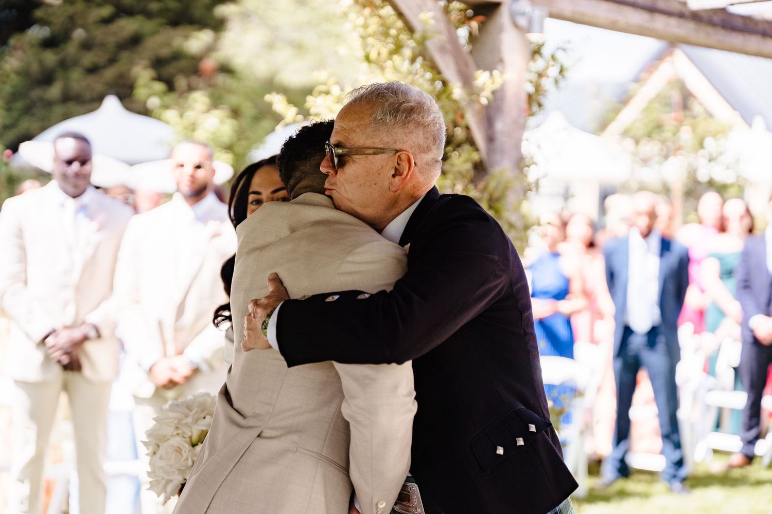 Emotional wedding embrace between bride and guests during outdoor ceremony with guests watching.