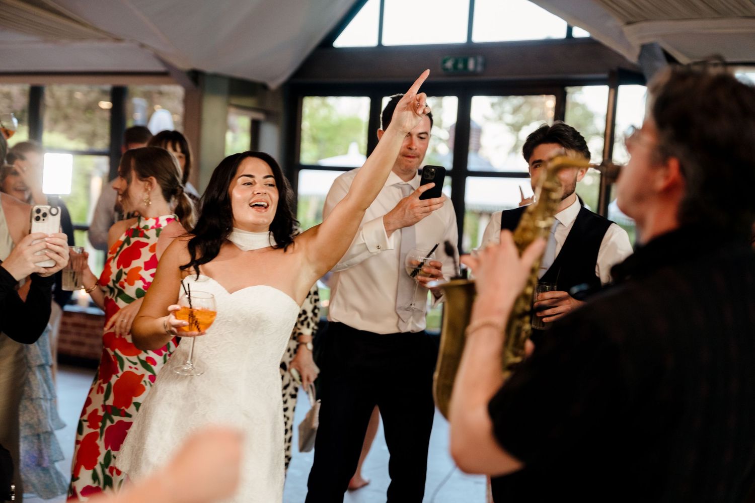 Bride in white dress laughs and dances with guests at energetic wedding reception with live band.