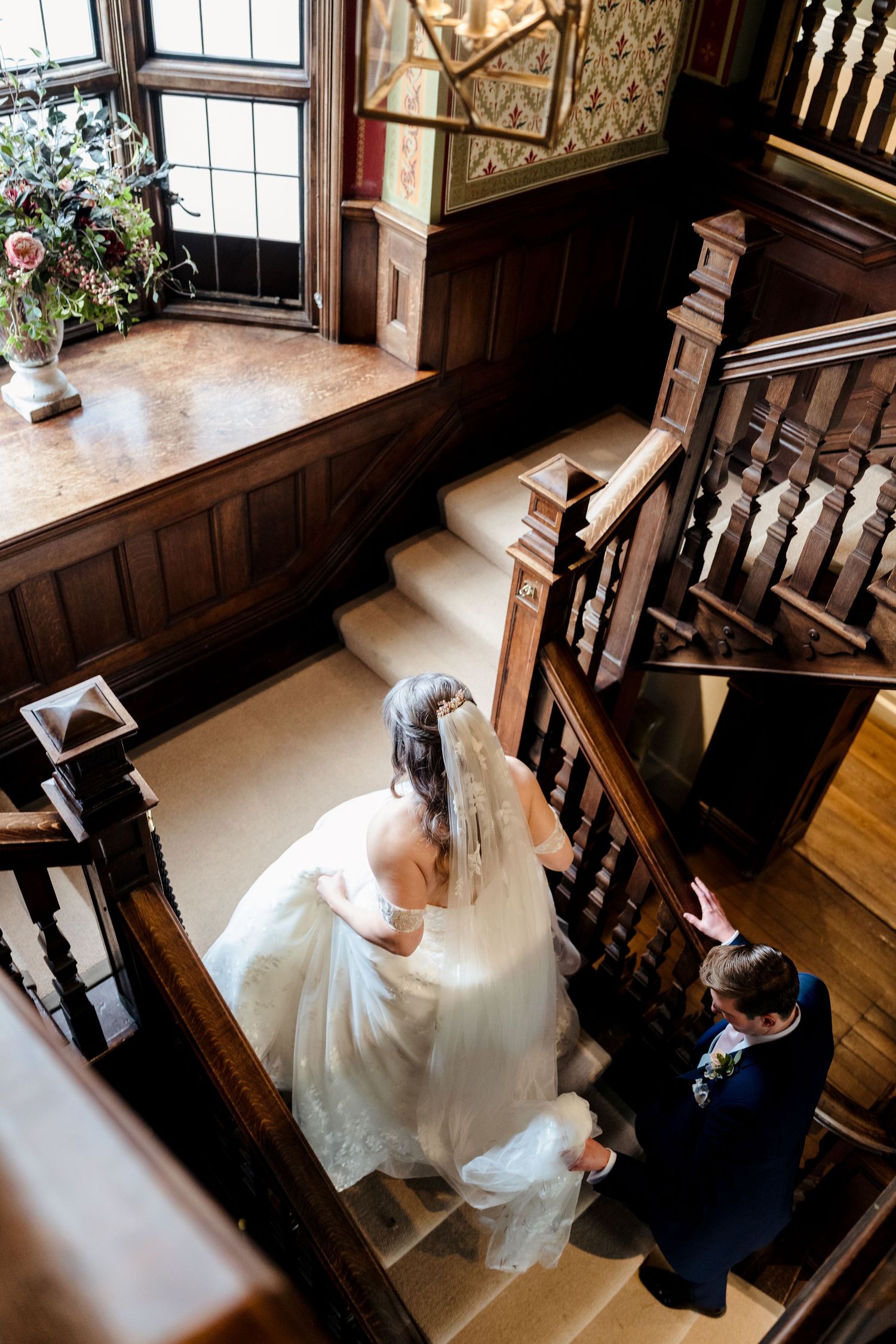 Aerial view of a bride and groom ascending an ornate wooden staircase in a historic wedding venue.