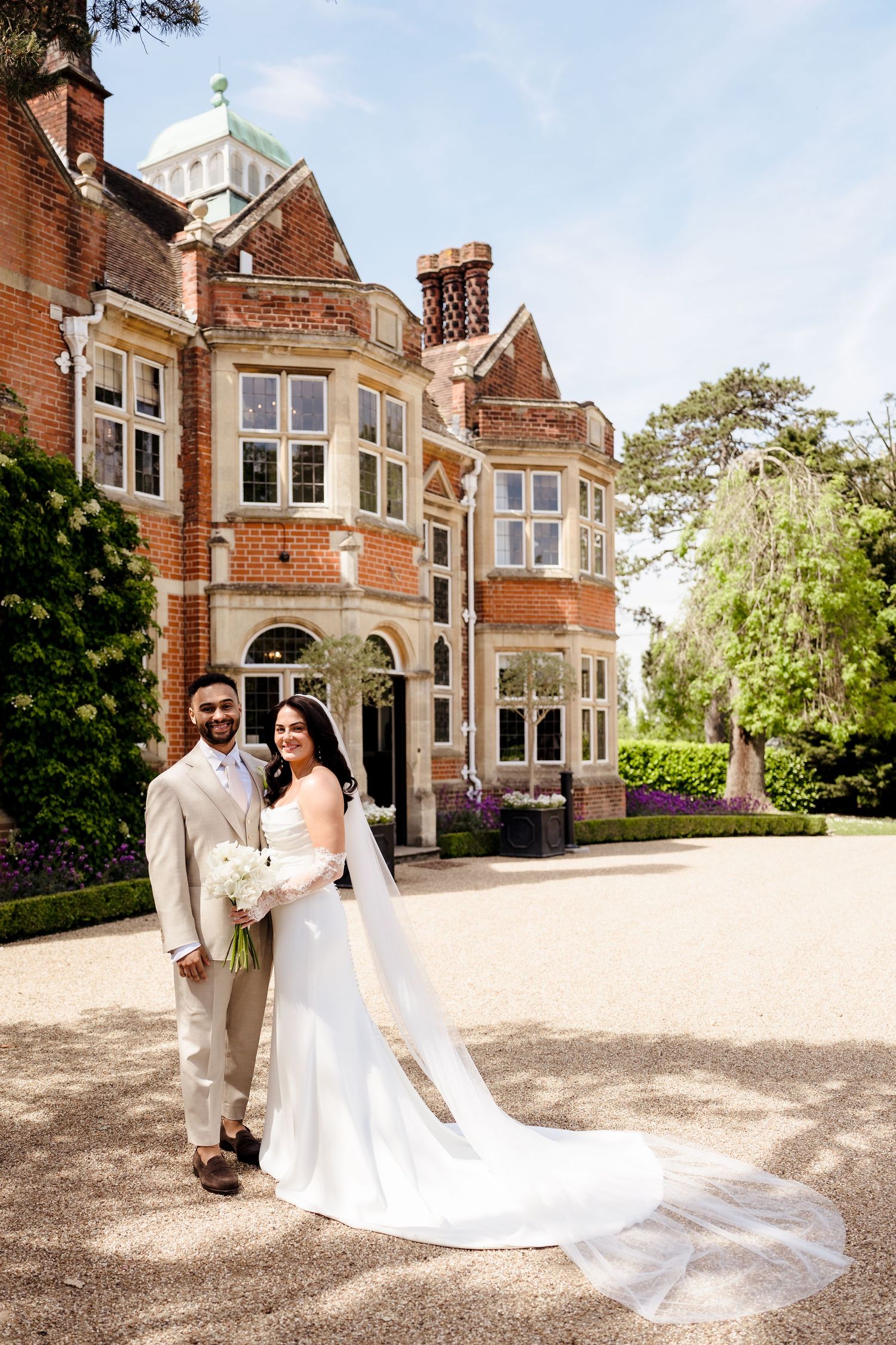 Bride and groom posing in front of a grand red brick English manor house on their wedding day.
