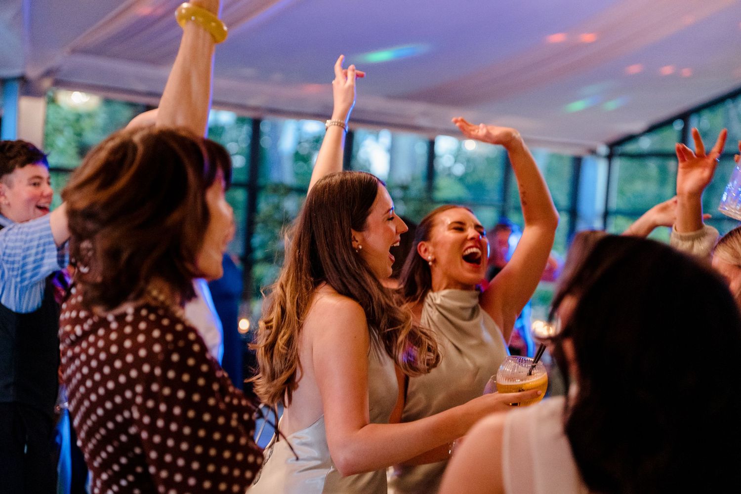 Guests dancing and laughing joyfully on the dance floor at a lively wedding reception party.