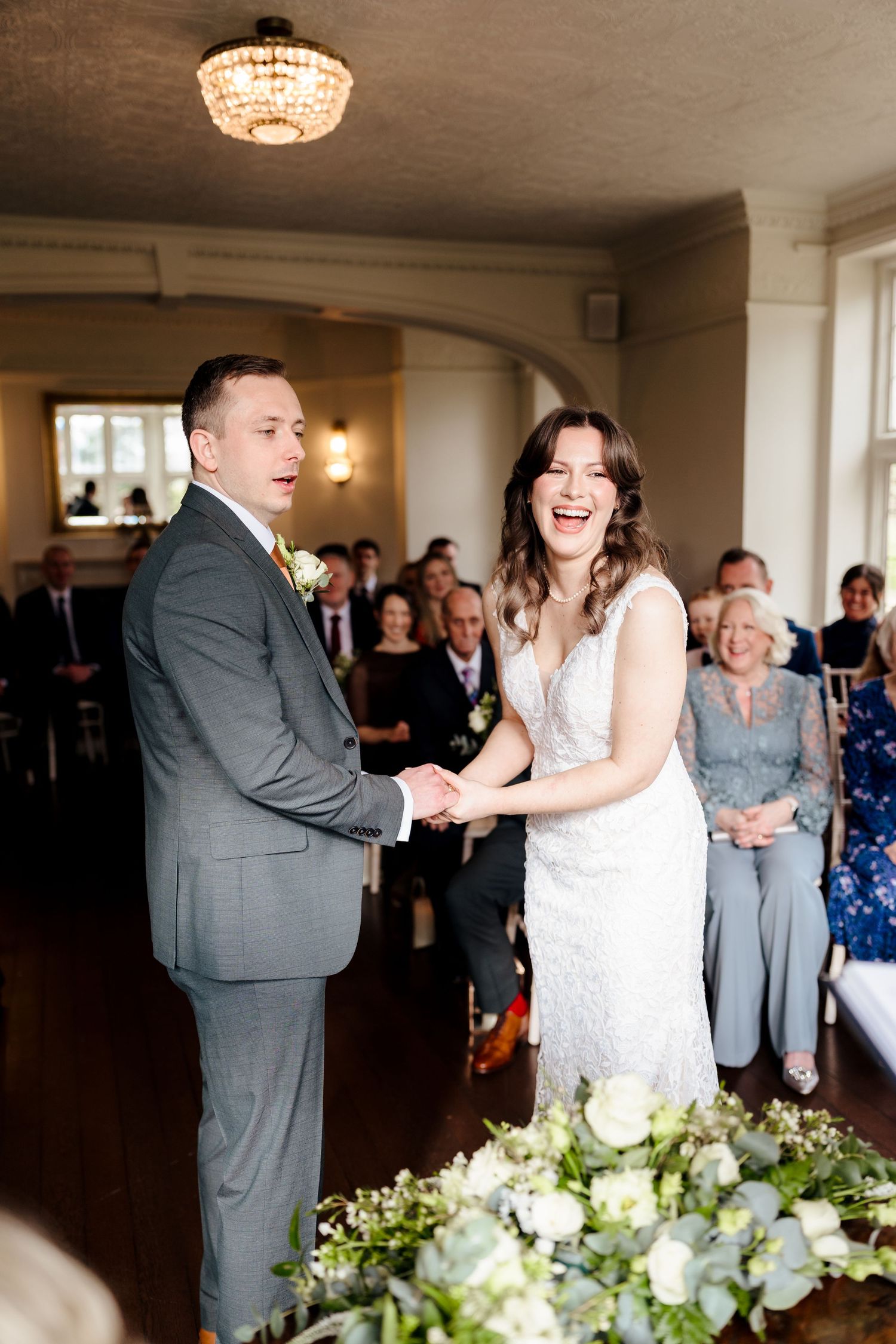 Bride and groom laughing joyfully while holding hands during their wedding ceremony in an elegant indoor venue.