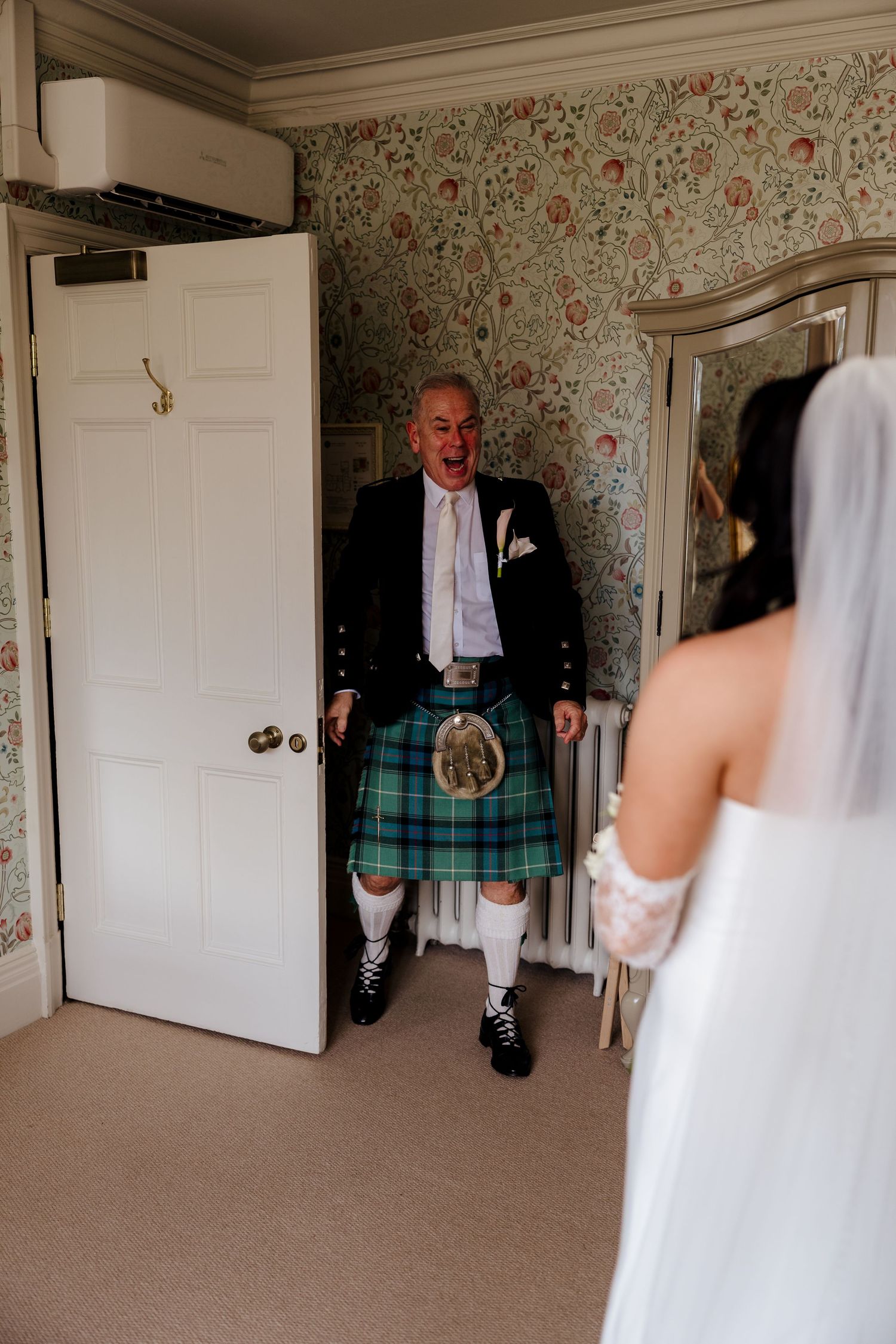 Father of the bride in traditional Scottish kilt reacting emotionally to seeing bride for first time.