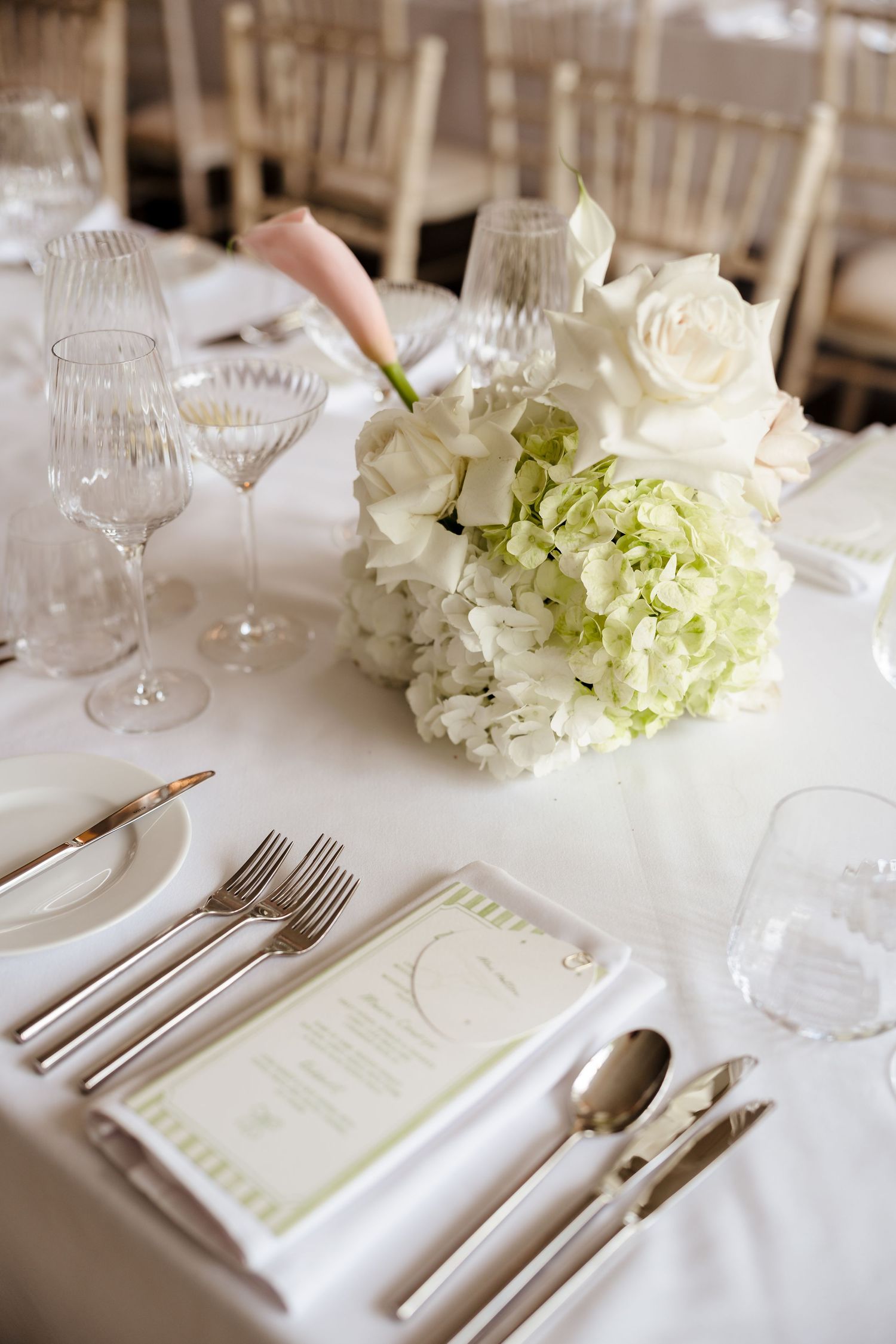 Elegant wedding reception table set with white hydrangeas, roses, crystal glasses, and formal place settings.