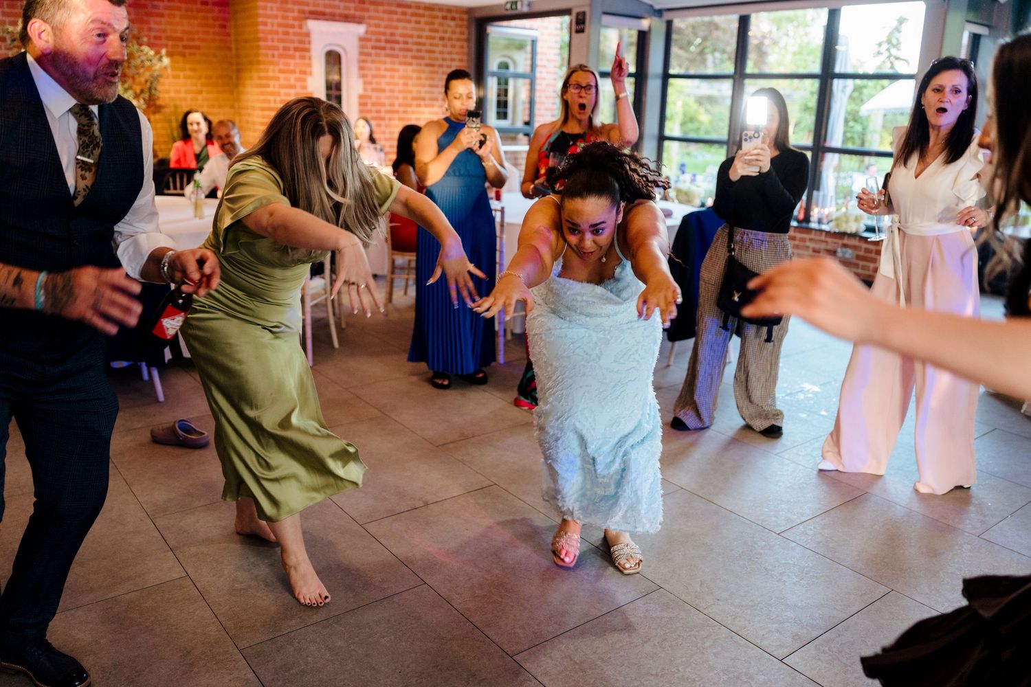Bride energetically dancing with guests at wedding reception in brick venue.
