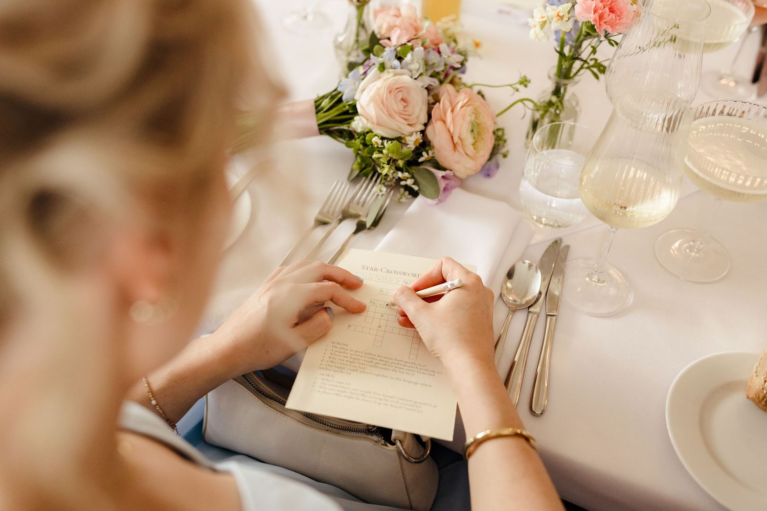 Guest writing on a wedding menu card at an elegantly set reception table with pink flowers.
