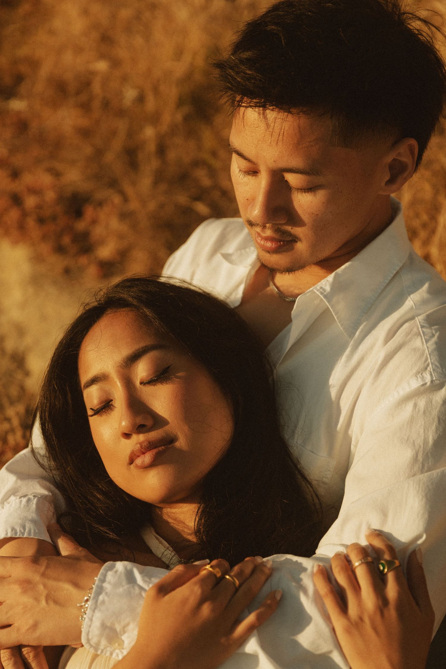 Romantic couple embracing in golden field, woman leaning back against man in white shirt, eyes closed.