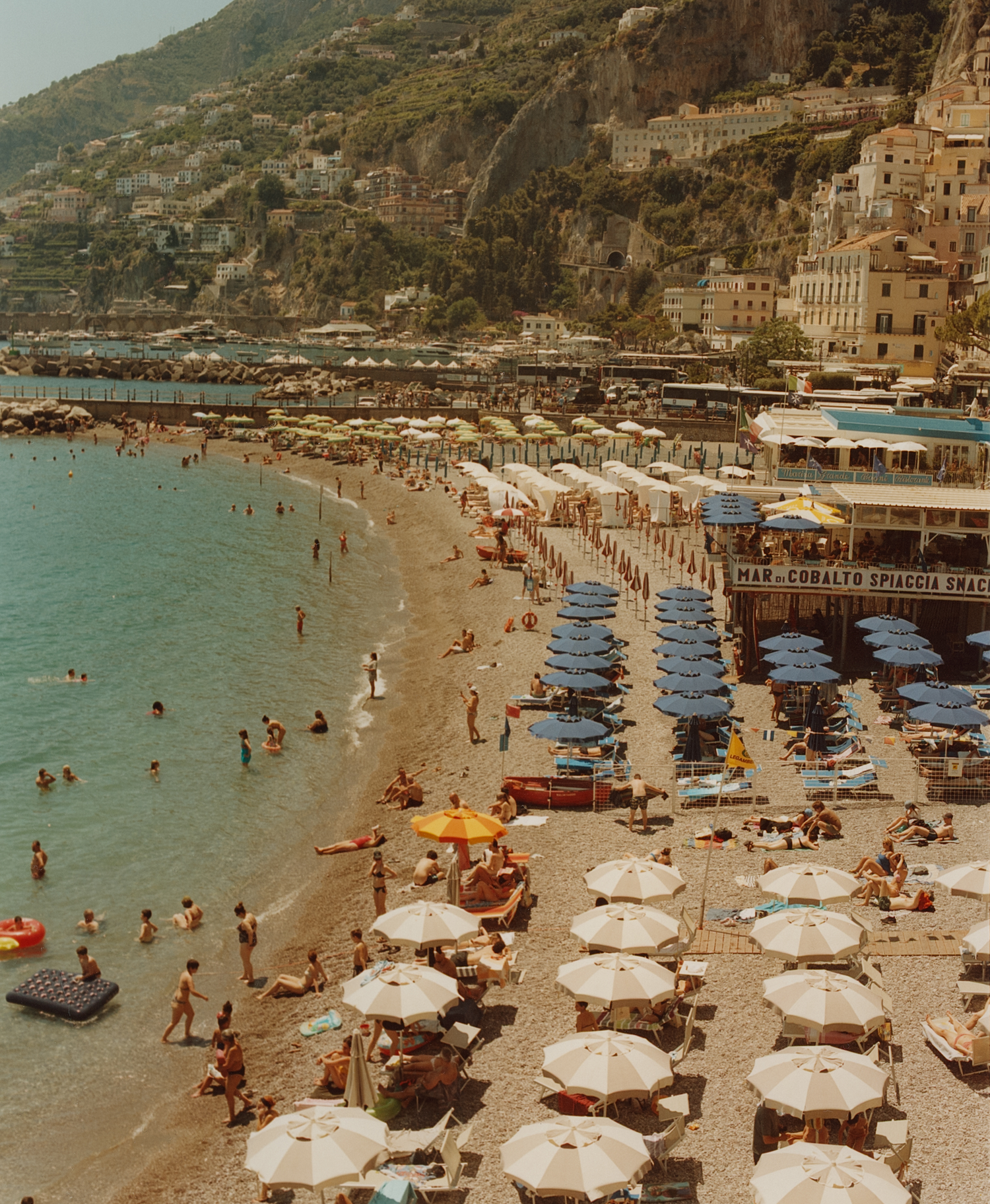 Crowded Italian beach resort with colorful umbrellas along the Amalfi Coast.