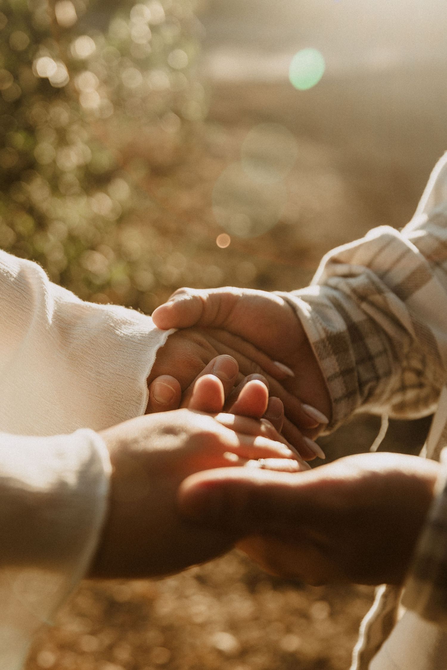 Two people holding hands tenderly in warm golden sunlight, symbolizing love and connection.