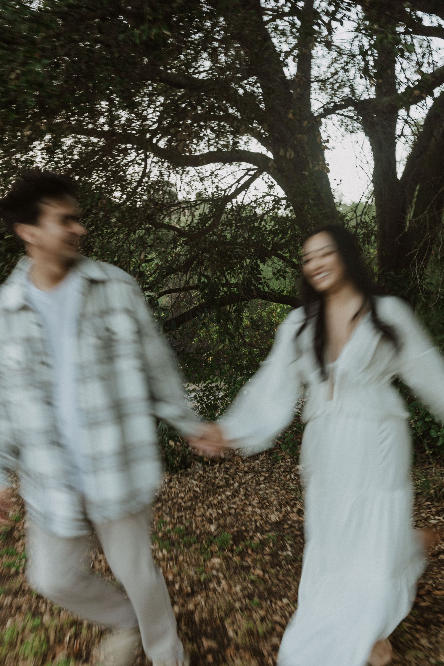 A blurred motion photo of a couple holding hands and walking through a lush green forest, woman in white dress.