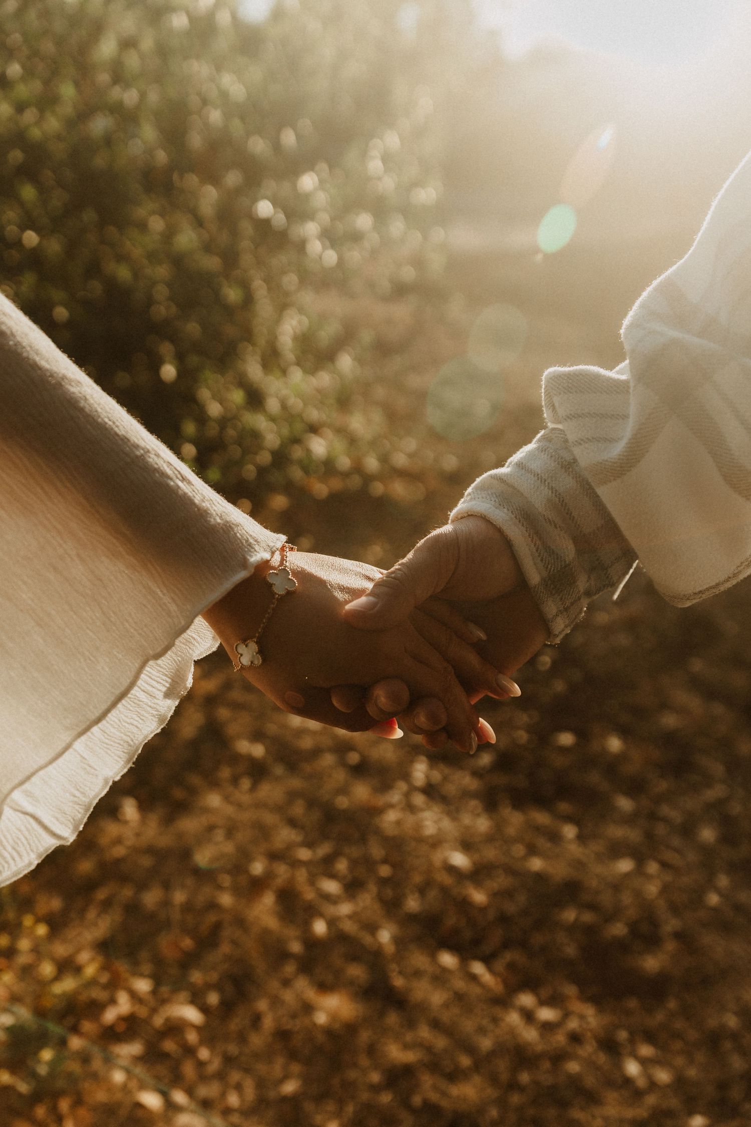 Two people holding hands in golden sunlight, one wearing a bracelet, surrounded by warm bokeh background.