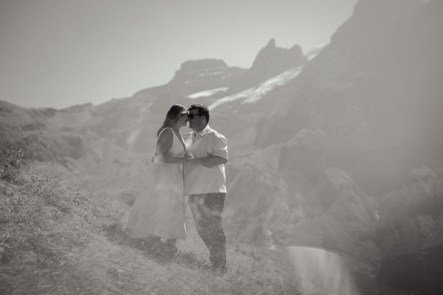 Black and white photo of a couple sharing a romantic kiss in a dramatic mountain landscape.