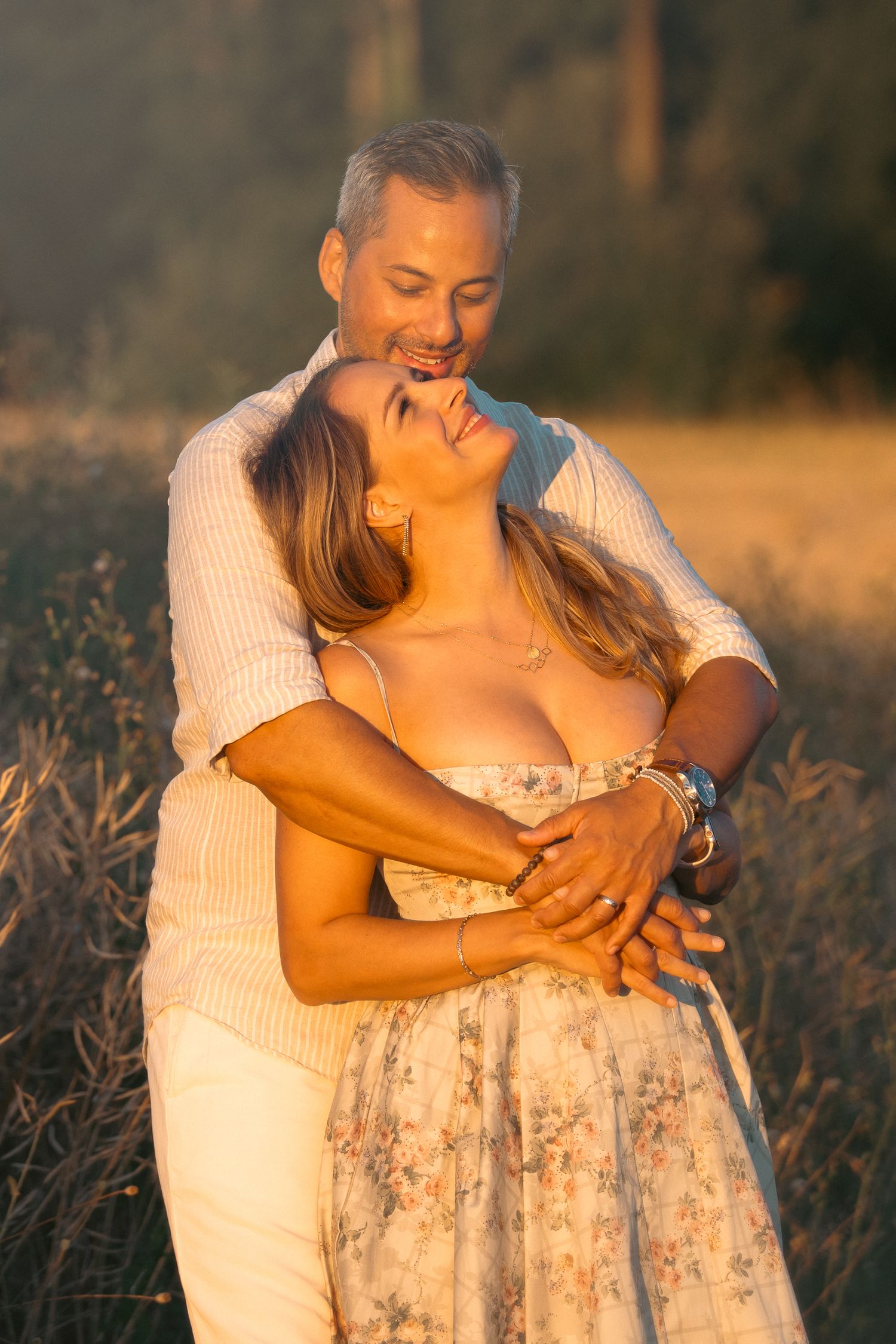 Happy couple hugging in a golden field at sunset, woman smiling joyfully.