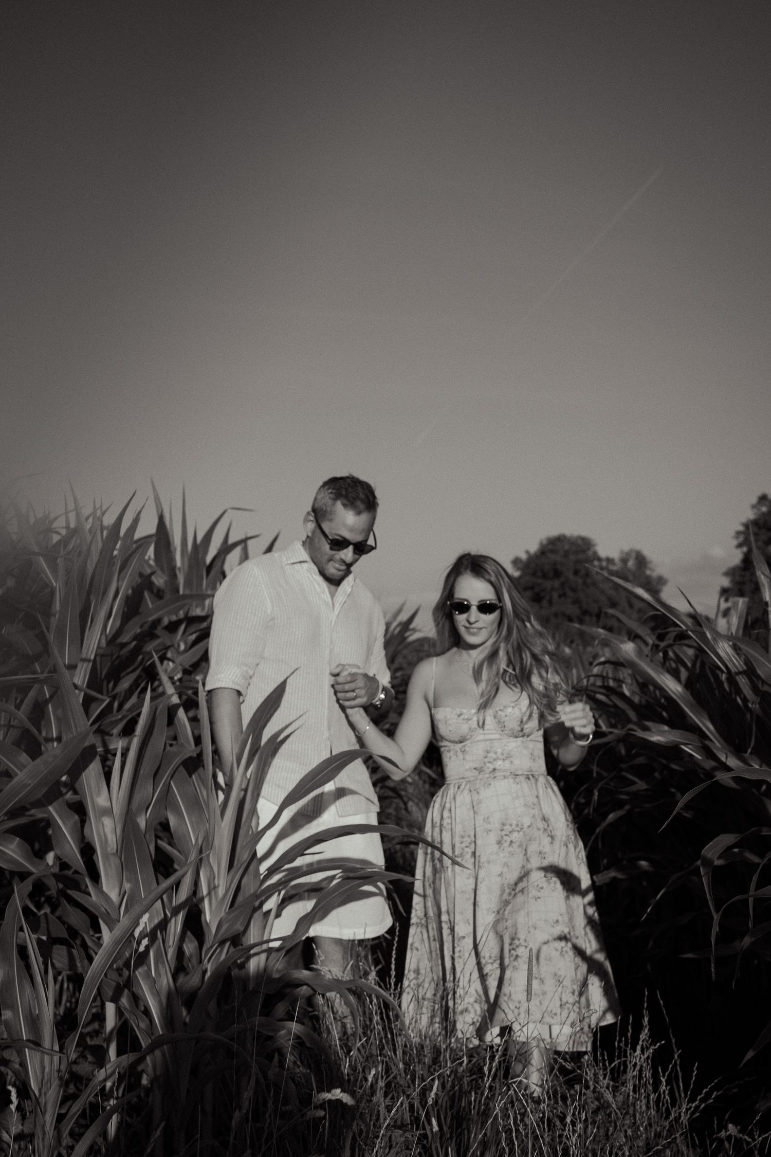Couple holding hands walking through tall green plants in a romantic black and white outdoor photo.