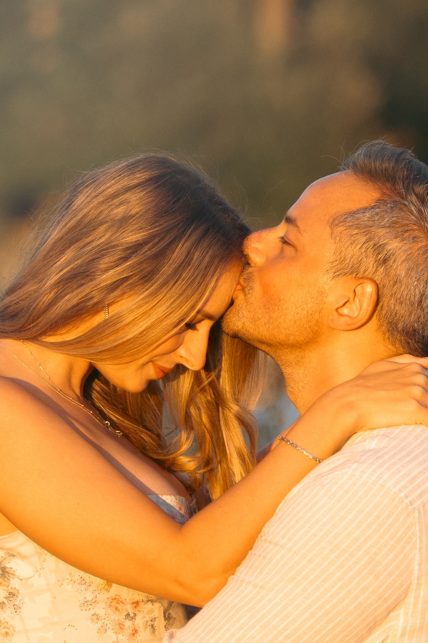 Couple embracing and kissing in warm golden sunset light outdoors.
