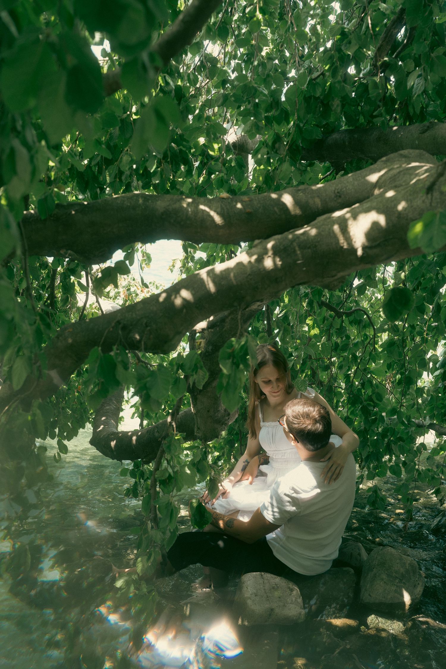 Two children sitting together under a large tree with lush green leaves in a serene outdoor setting.