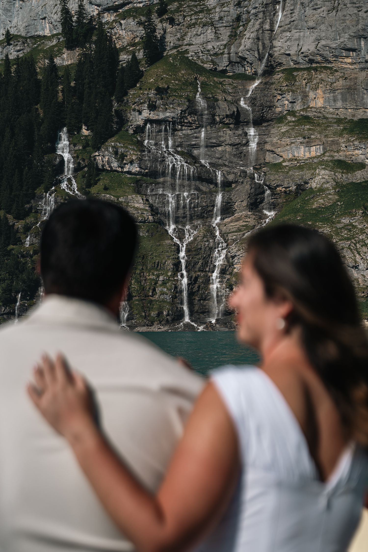 A couple embraces while admiring stunning waterfalls cascading down rocky alpine cliffs.