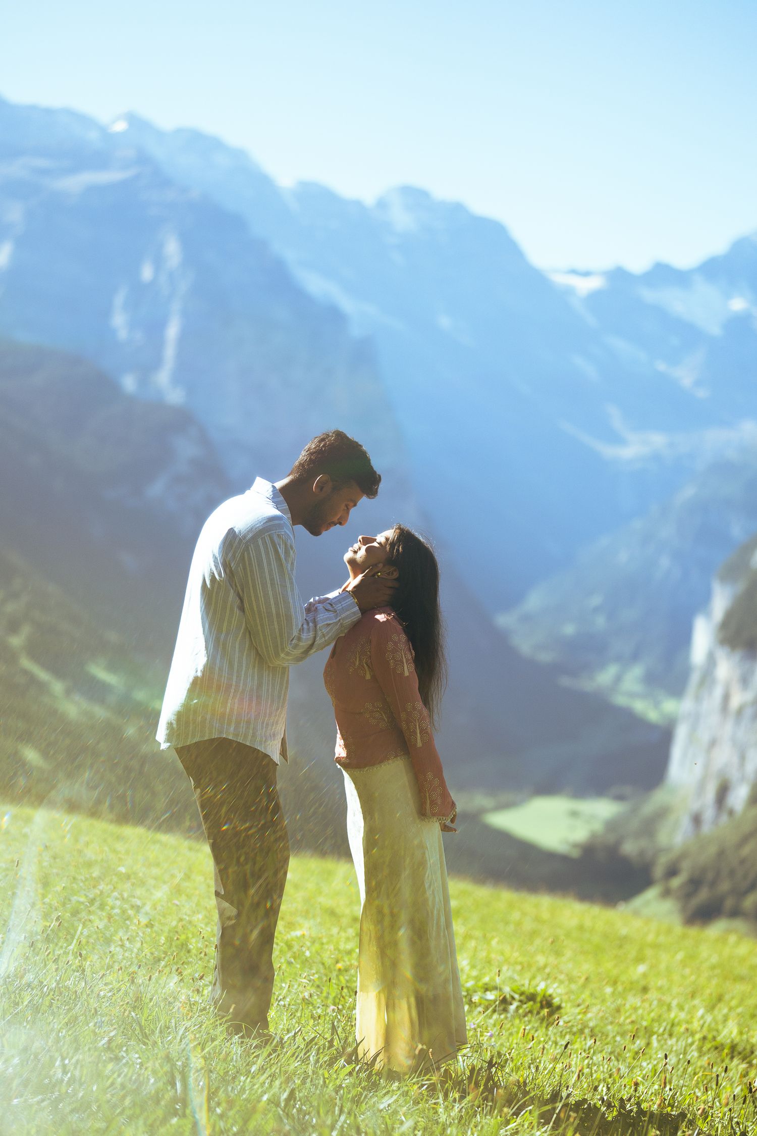 Romantic couple sharing a tender moment on a lush alpine meadow with stunning mountain backdrop.