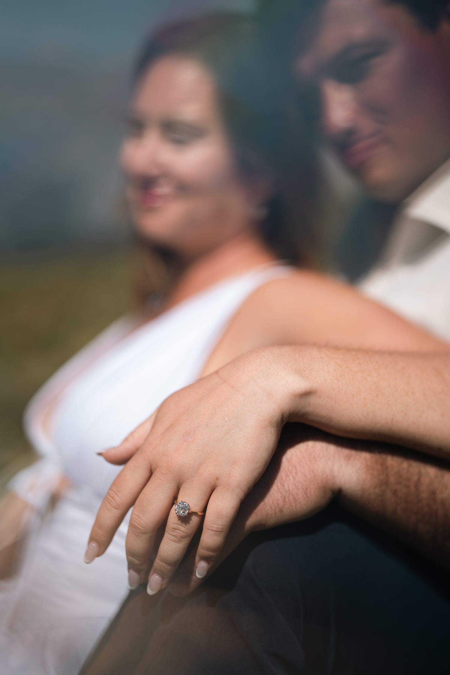 Close-up of an engagement ring on a woman's hand as a couple sits together in a romantic outdoor setting.