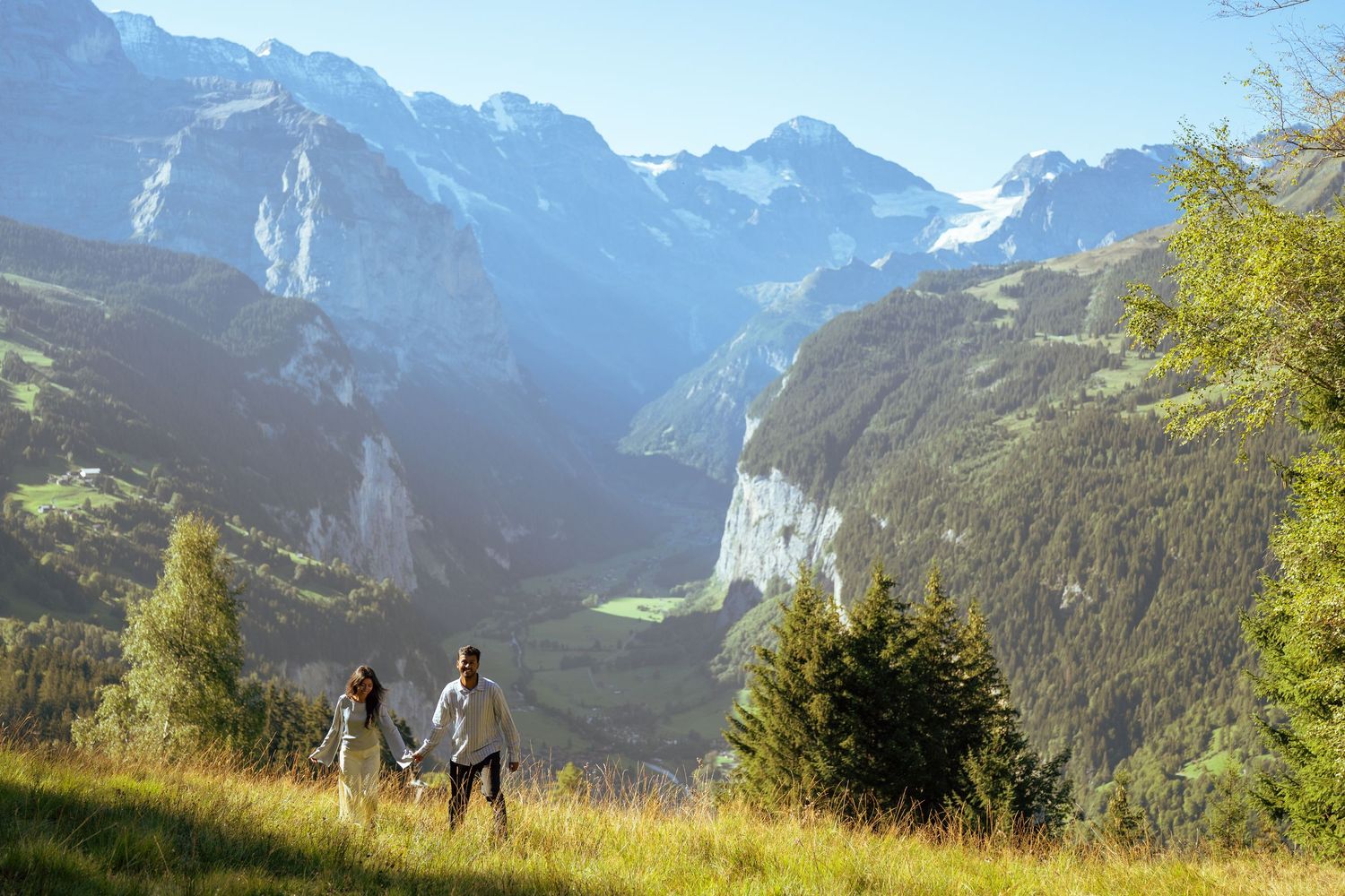 Couple holding hands on alpine meadow with panoramic view of Lauterbrunnen valley and Swiss Alps mountains.