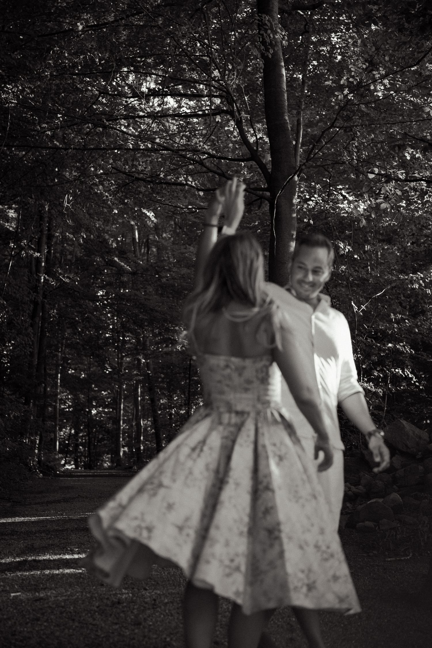 Black and white photo of couple dancing on a forest path, man smiling at partner.
