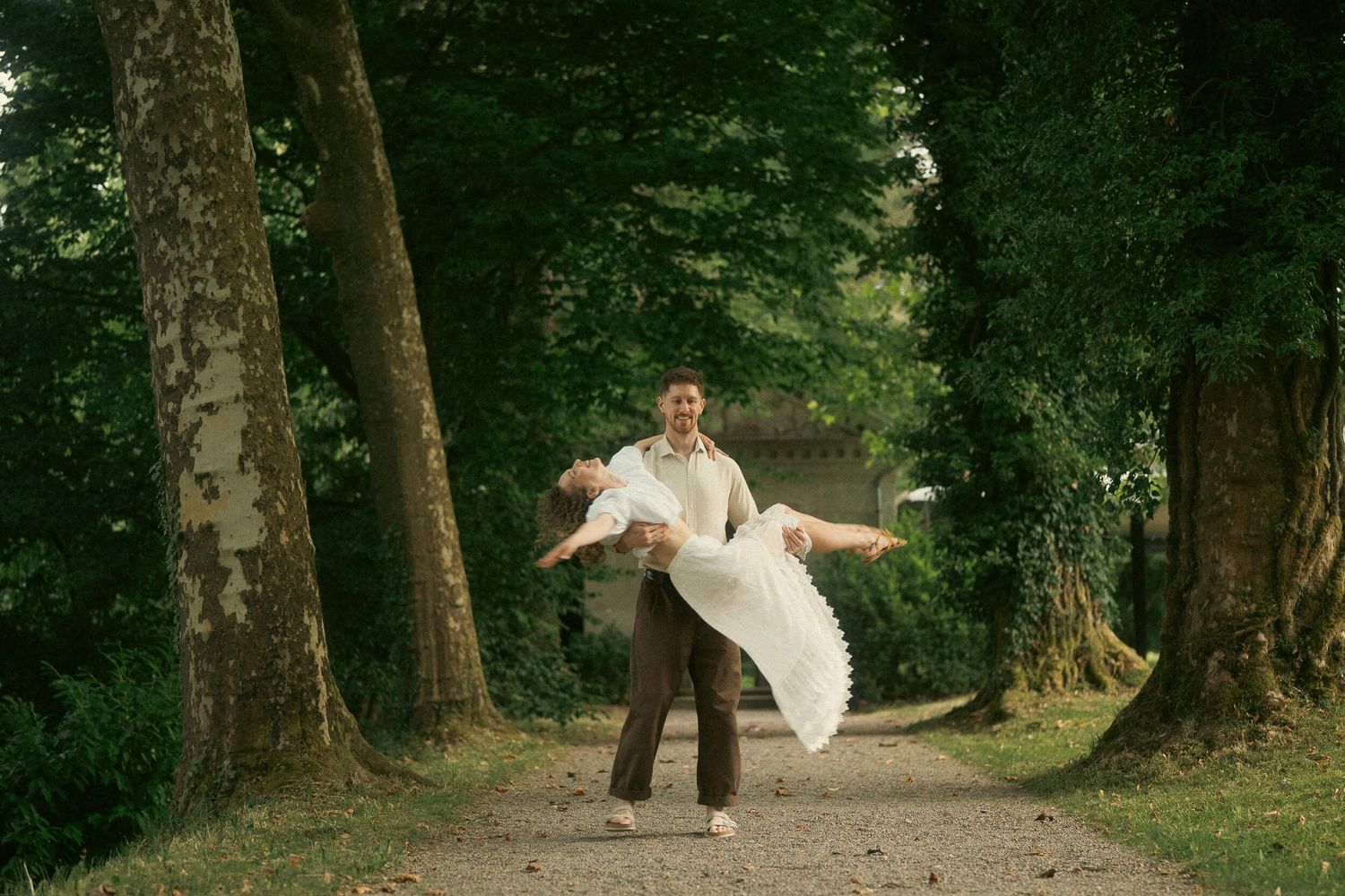 Couple dancing joyfully on a tree-lined path, groom lifting bride in white dress outdoors. Villa Boveri Wedding, Baden, Wedding Photography