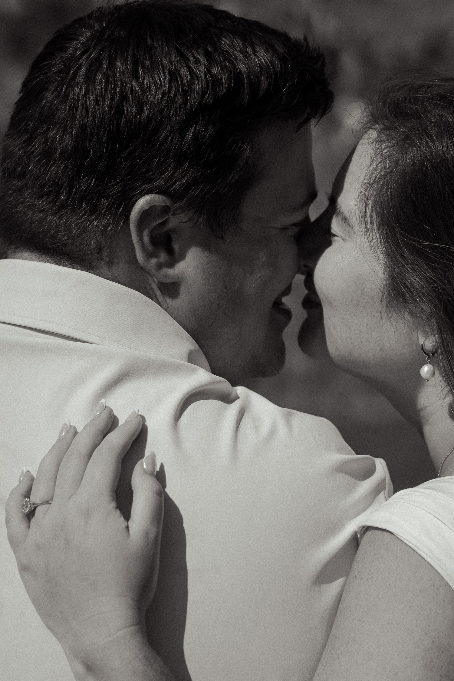 A romantic black and white close-up of a couple about to kiss, bride wearing a diamond ring.
