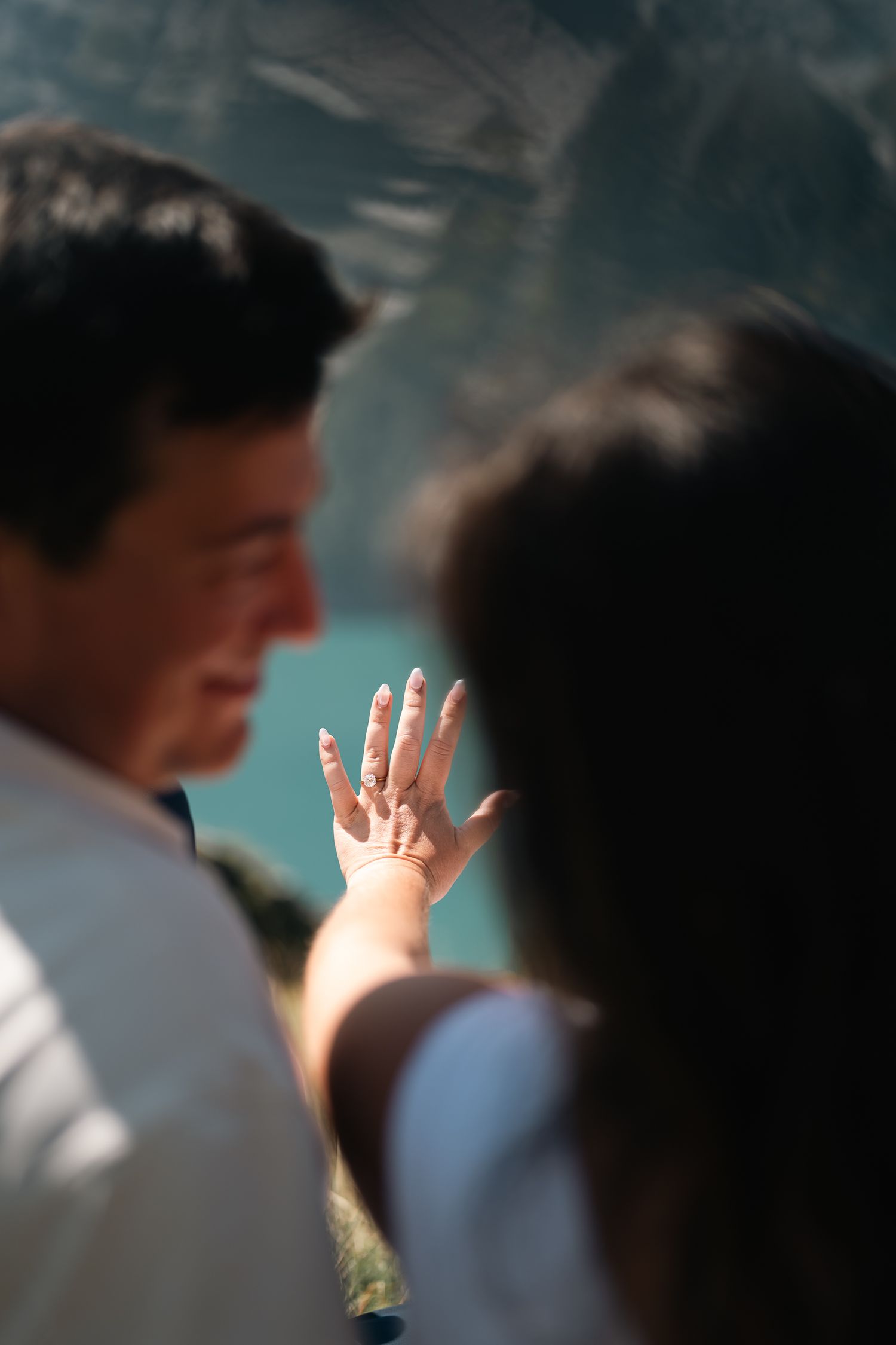 A woman shows off her engagement ring while a man looks on at an aquarium.
