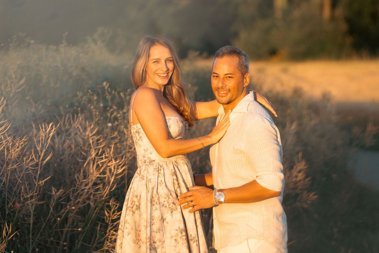 Happy couple embracing in a golden sunset field, smiling at the camera.