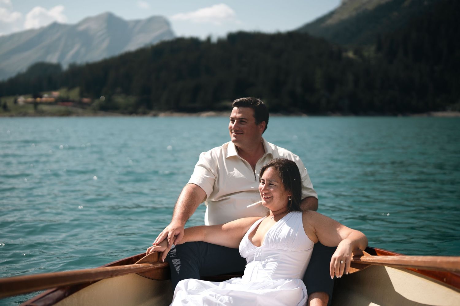 Couple relaxing on a wooden rowboat on a serene alpine lake with mountains in the background.